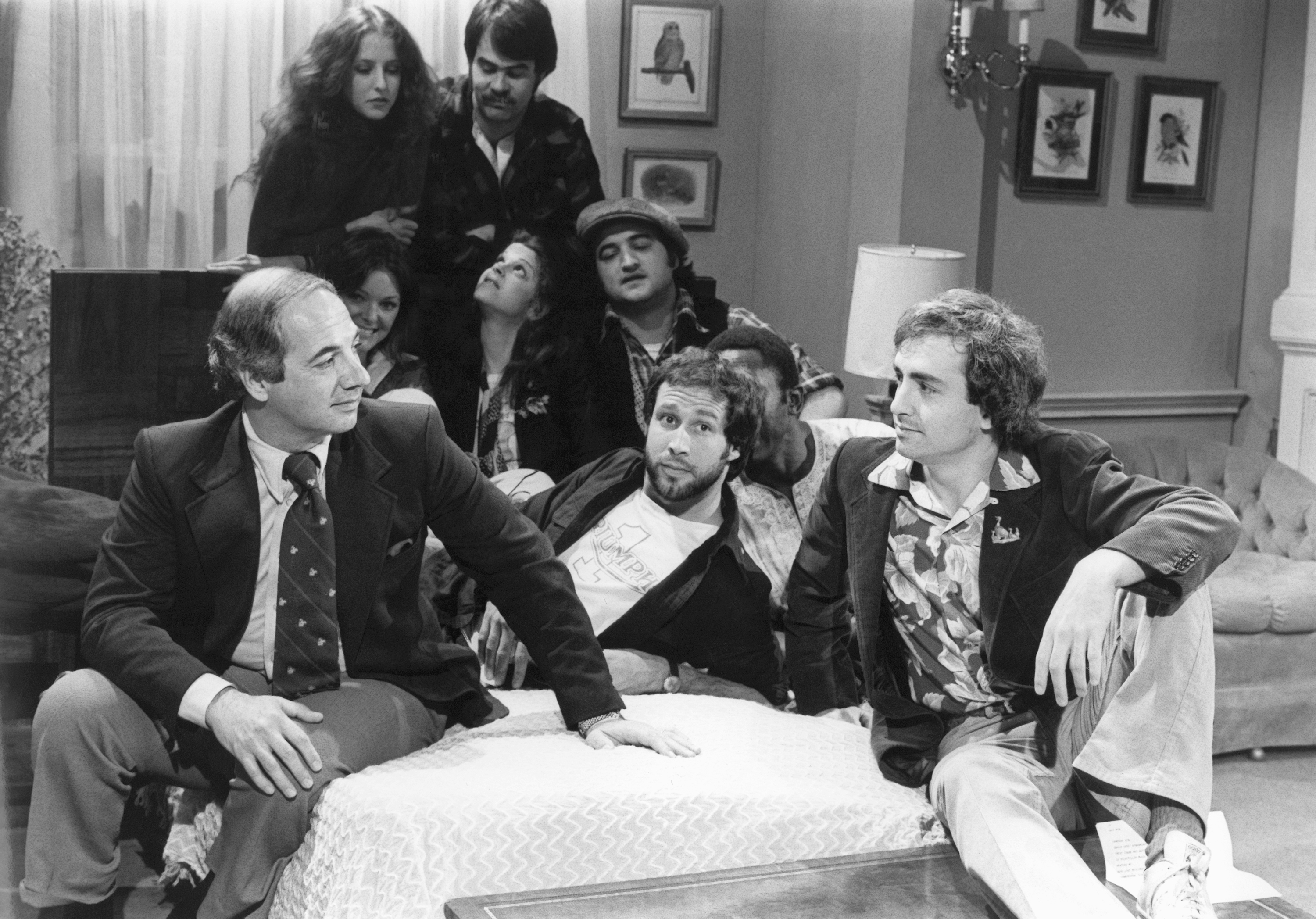 White House Press Secretary Ron Nessen, left, appears on the "Saturday Night Live" set with producer Lorne Michaels, right, and cast members Chevy Chase, foreground center, Laraine Newman, background left, Dan Aykroyd, background right, Jane Curtin, second row from left, Gilda Radner, John Belushi and Garret Morris, partially obscured, on April 17, 1976, in New York.