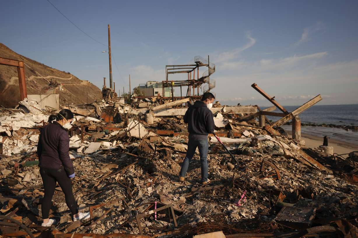 Tony Lai, center, rakes through the remains of his fire-ravaged beachfront property with his wife Everlyn in the aftermath of the Palisades Fire on Jan. 28, in Malibu, Calif.