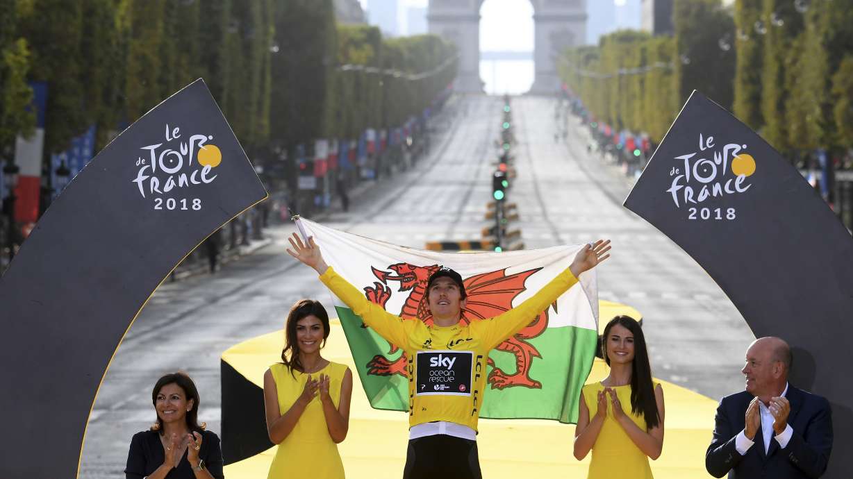FILE - Tour de France winner Britain's Geraint Thomas, wearing the overall leader's yellow jersey, and draped in the flag of Wales celebrates on the podium after the twenty-first stage of the Tour de France cycling race over 116 kilometers (72.1 miles) with start in Houilles and finish on Champs-Elysees avenue in Paris, France, Sunday July 29, 2018.