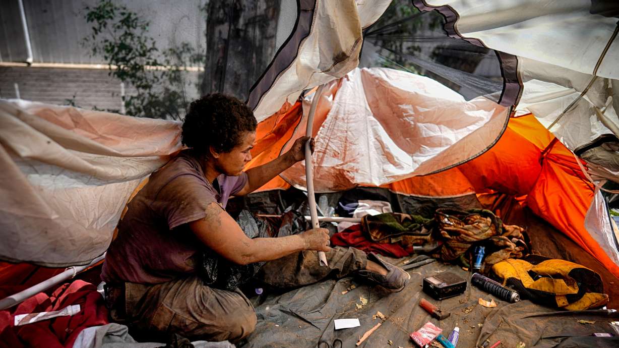 Esca Guernon fixes her tent at an encampment next to the 405 Freeway in the Van Nuys section of Los Angeles on July 26, 2024. The California governor issued an order directing state agencies to clear homeless encampments from state land.