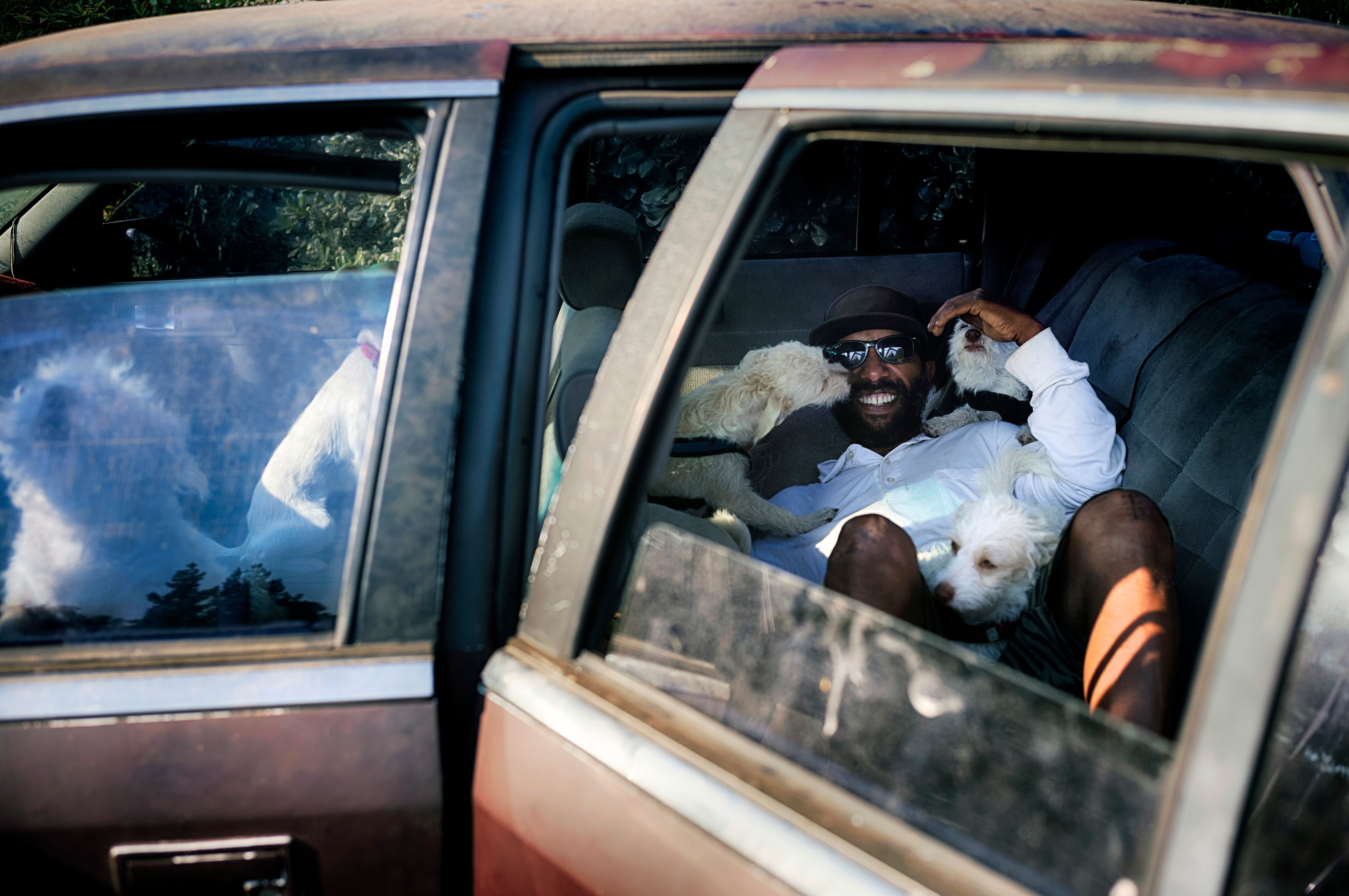 David Clarke, who is suffering from homelessness and living in his car, cuddles with his six dogs early morning in a parking lot in Los Angeles on July 9, 2024.