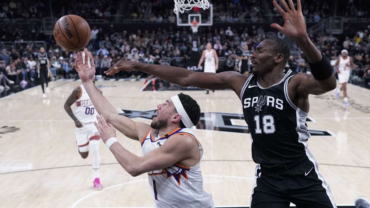 Phoenix Suns guard Devin Booker (1) is defended by San Antonio Spurs center Bismack Biyombo (18) as he tries to score during the second half of an NBA basketball game in Austin, Texas, Thursday, Feb. 20, 2025.