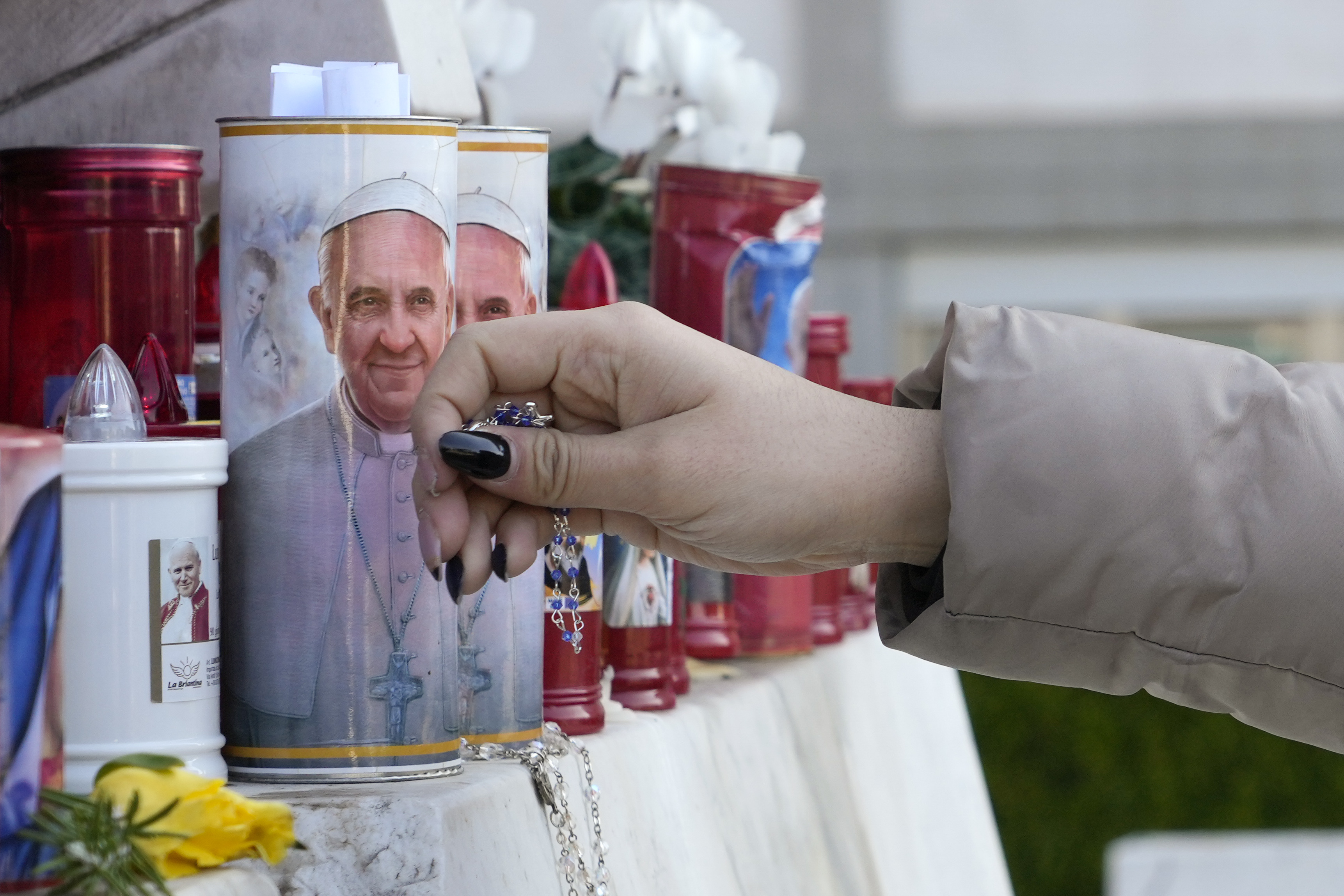 A woman lays a rosary near candles adorned with pictures of Pope Francis in Rome, Saturday. The Vatican says Pope Francis is in critical condition.