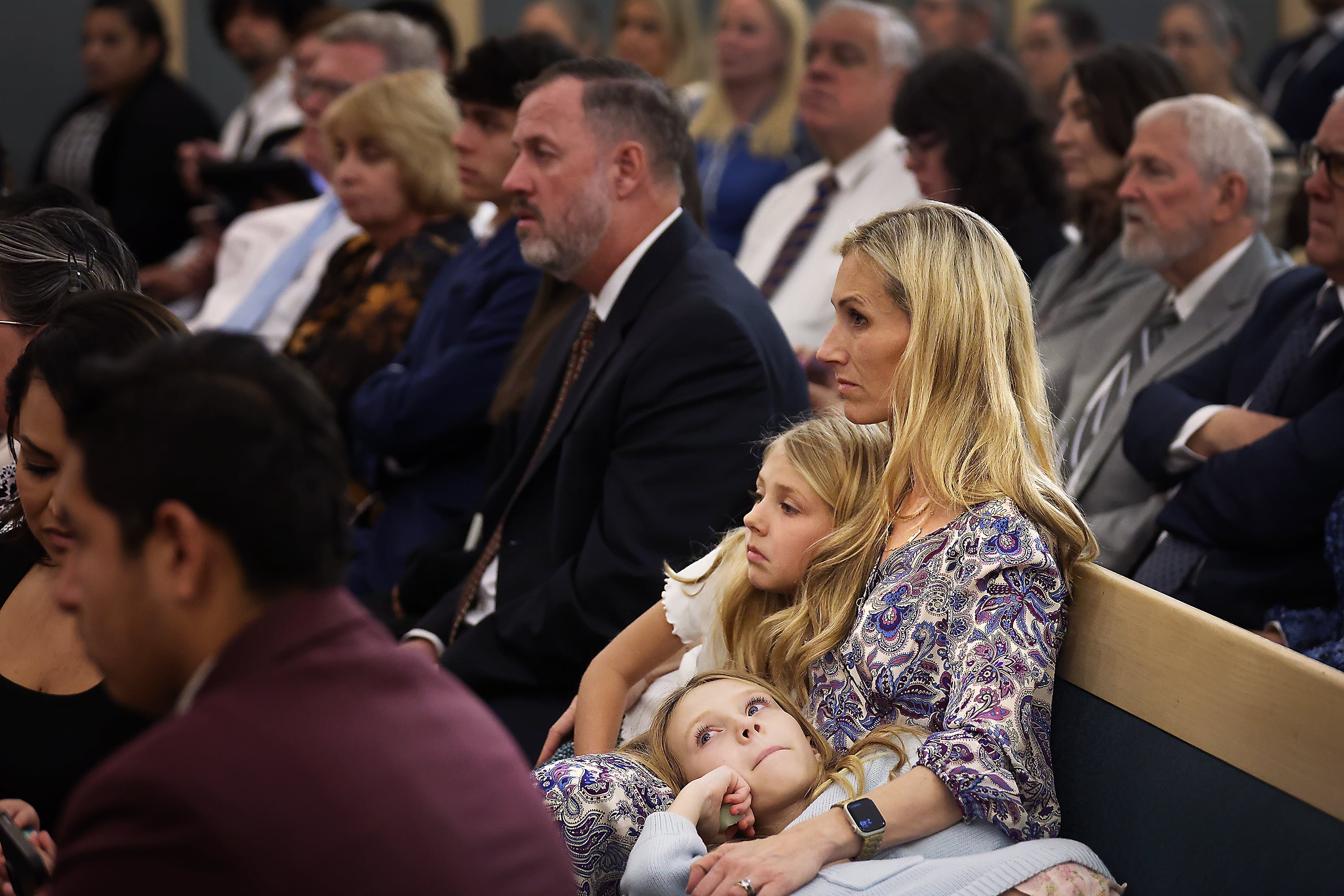 Hilary Cannon, 40, who lost her home in the recent Southern California wildfires, listens to President Jeffrey R. Holland at the San Fernando California Stake Center on Saturday, in Van Nuys, Calif. Two of Cannon's children, Marigold, 8, and Ada Grace, 10, snuggle with her and listen in as well.