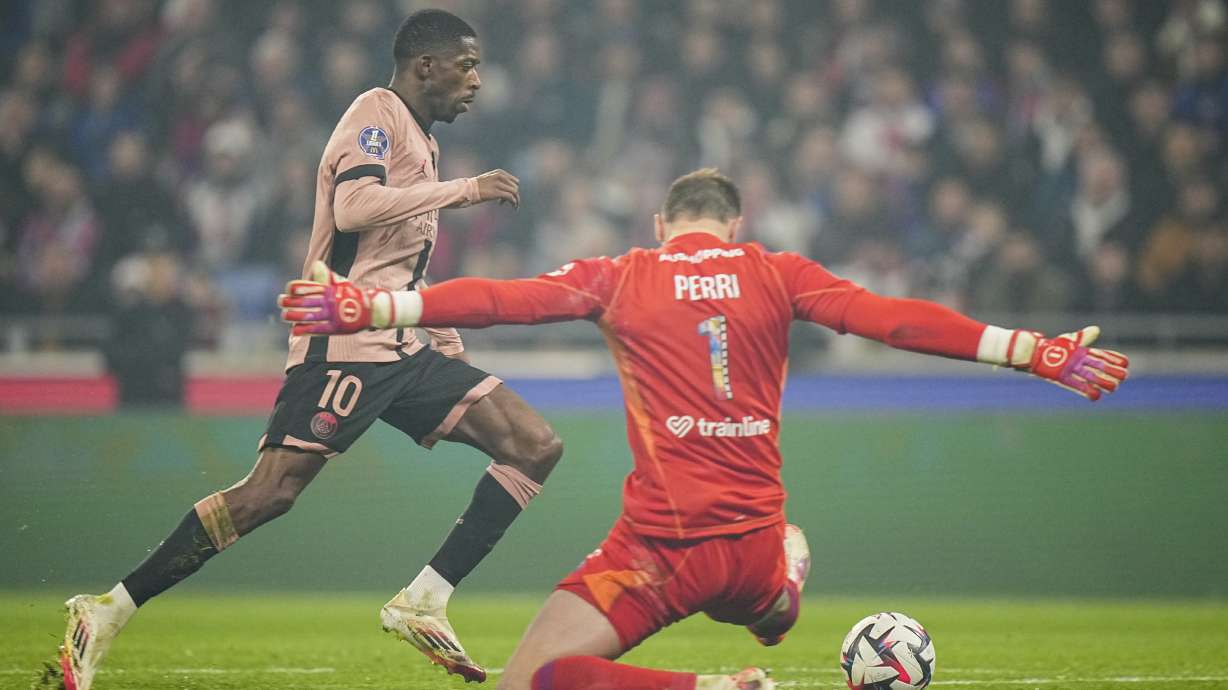Lyon's goalkeeper Lucas Perri, right, makes a save in front of PSG's Ousmane Dembele during the French League One soccer match between Lyon and Paris Saint-Germain at the Groupama stadium, outside Lyon, France, Sunday, Feb. 23, 2025.