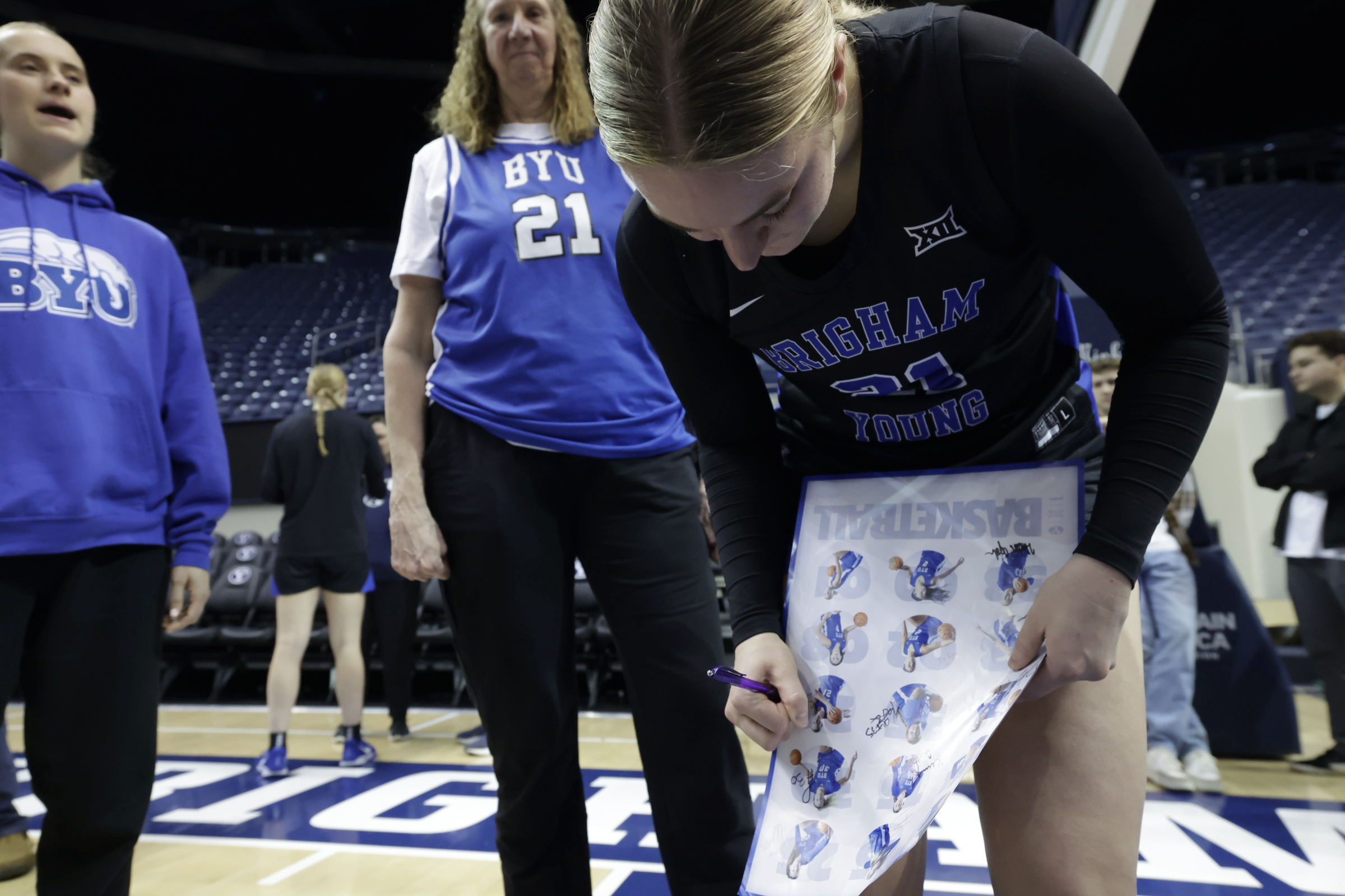 Former BYU women's basketball Tresa Spaulding Hamson looks on as her daughter Heather, a junior on the 2024-25 team, signs a poster after a Big 12 women's basketball game against Kansas, Tuesday, Feb. 25, 2025 at the Marriott Center in Provo, Utah. - BYU Photo