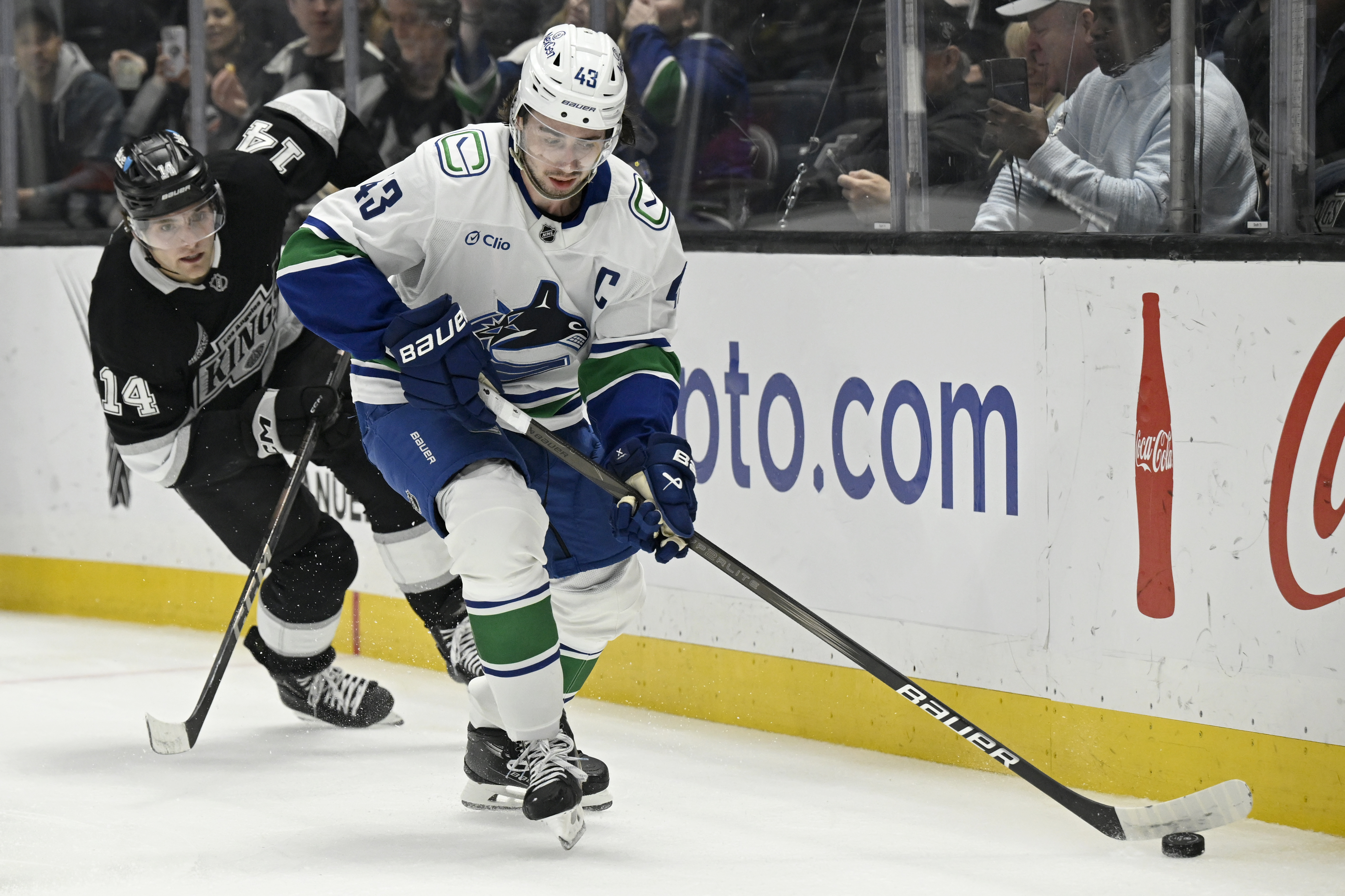 Vancouver Canucks defenseman Quinn Hughes (43) controls the puck with Los Angeles Kings right wing Alex Laferriere (14) in pursuit during the first period of an NHL hockey game in Los Angeles, Wednesday, Feb. 26, 2025. 