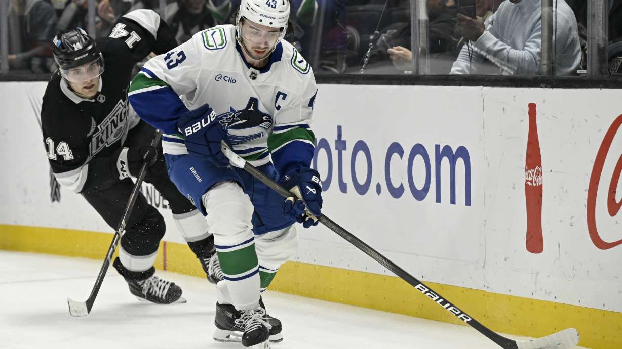 Vancouver Canucks defenseman Quinn Hughes (43) controls the puck with Los Angeles Kings right wing Alex Laferriere (14) in pursuit during the first period of an NHL hockey game in Los Angeles, Wednesday, Feb. 26, 2025.