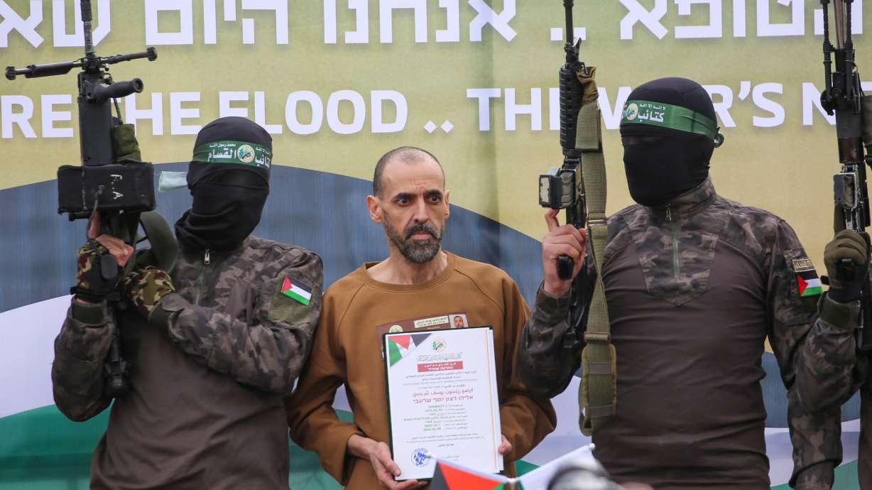 Hamas fighters escort Israeli hostage Eli Sharabi on a stage before handing him over to a Red Cross team in Deir el-Balah, central Gaza, on Feb. 8. Israel and Hamas remain split on what's next after the first phase of the Gaza ceasefire ends.