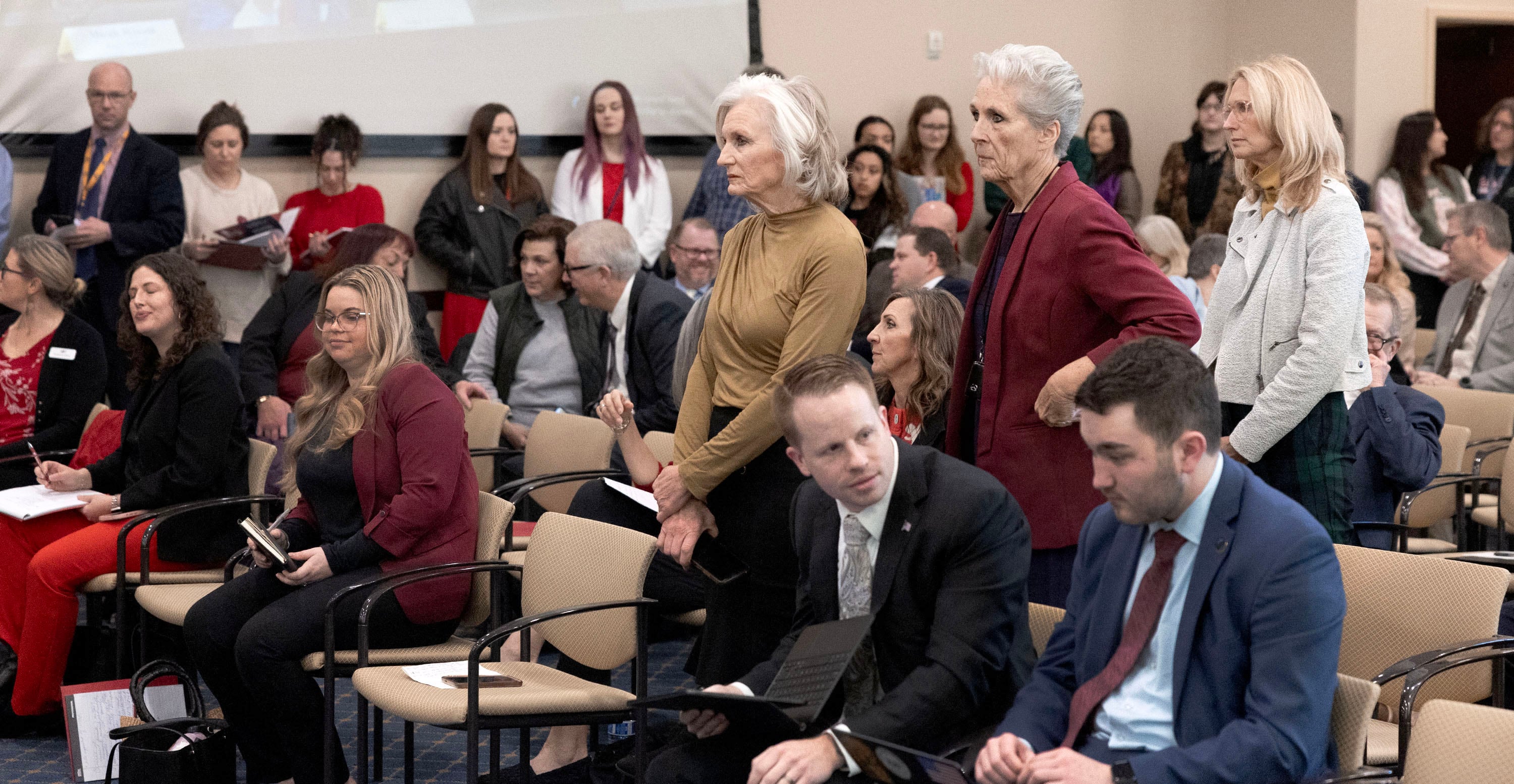 Three women wait to speak in favor of HB77, Flag Display Amendments, while those opposed line the wall during a Senate Education Committee meeting at the Capitol in Salt Lake City on Friday.