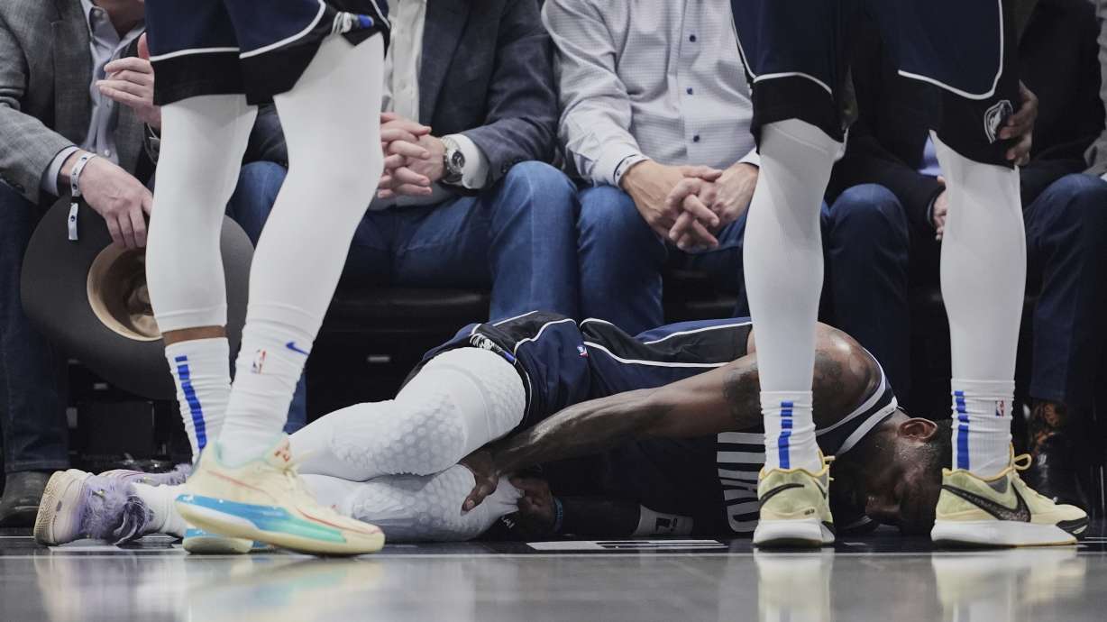 Dallas Mavericks' Kyrie Irving holds onto his leg after suffering an unknown injury as teammates stand by in the first half of an NBA basketball game against the Sacramento Kings in Dallas, Monday, March 3, 2025.