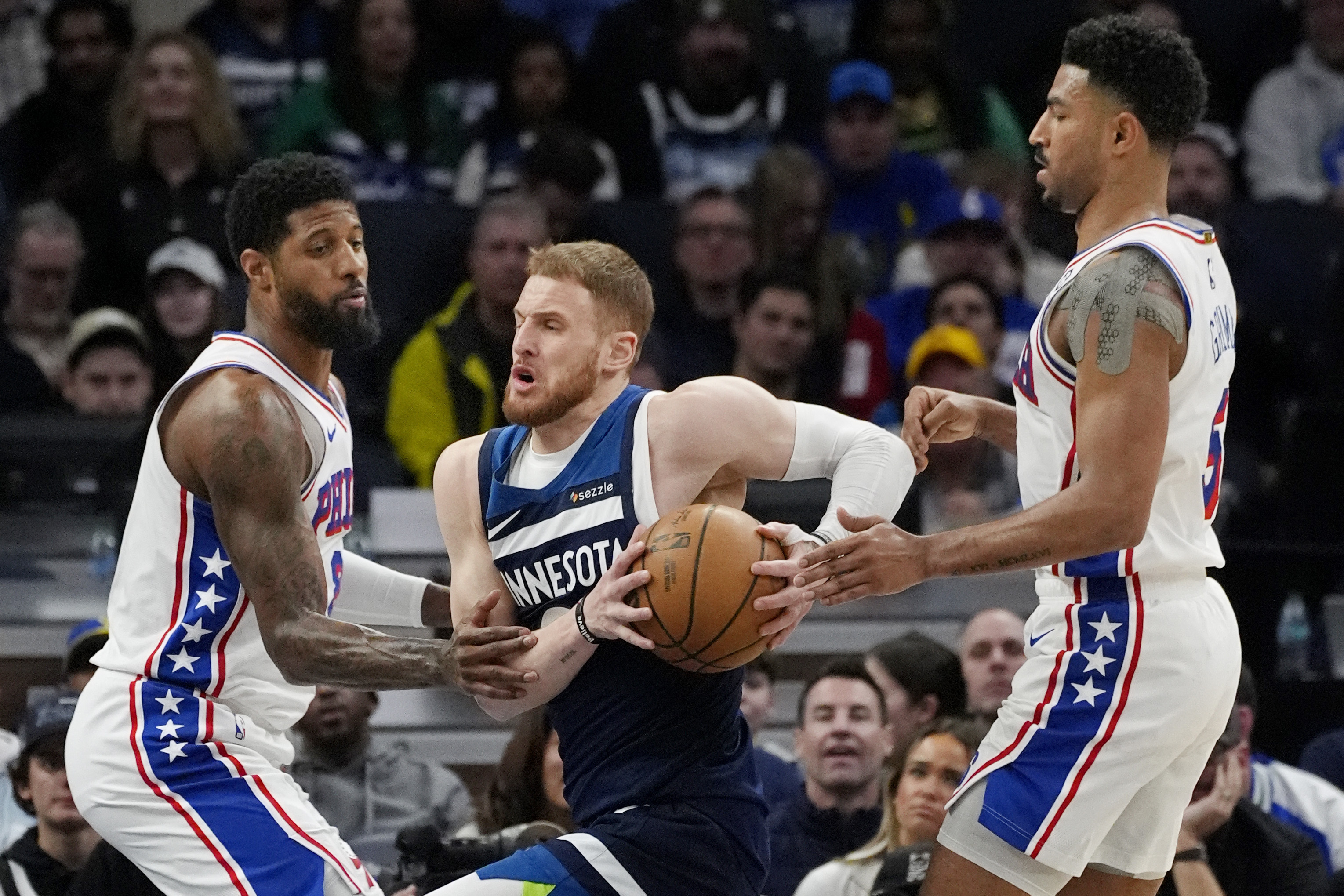Minnesota Timberwolves guard Donte DiVincenzo, middle, drives to the basket between Philadelphia 76ers forward Paul George, left, and guard Quentin Grimes, right, in the first quarter of an NBA basketball game Tuesday, March 4, 2025, in Minneapolis. 