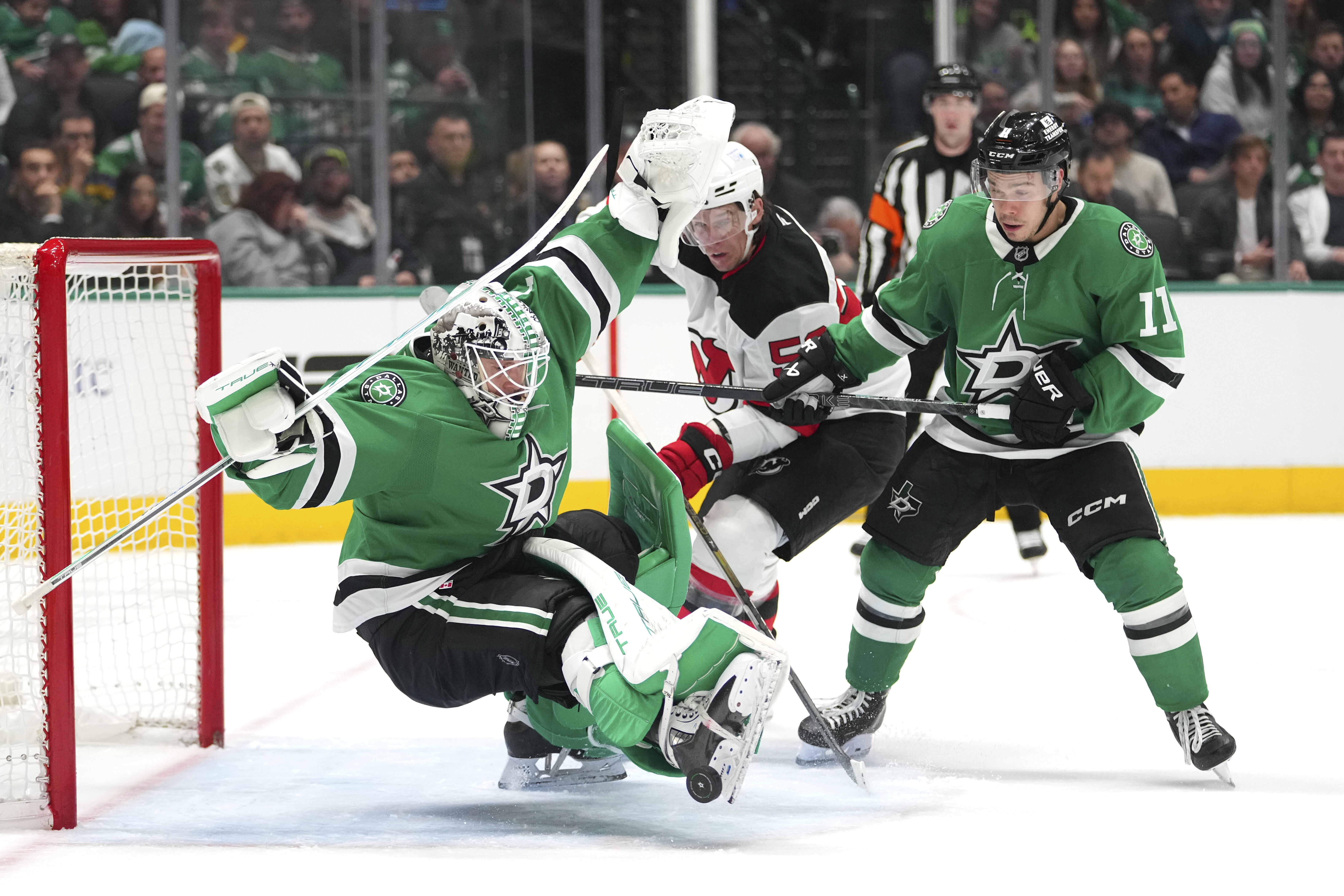 Dallas Stars goaltender Casey DeSmith, left, falls to the ice while defending against New Jersey Devils left wing Erik Haula, center, during the second period of an NHL hockey game Tuesday, March 4, 2025, in Dallas. 