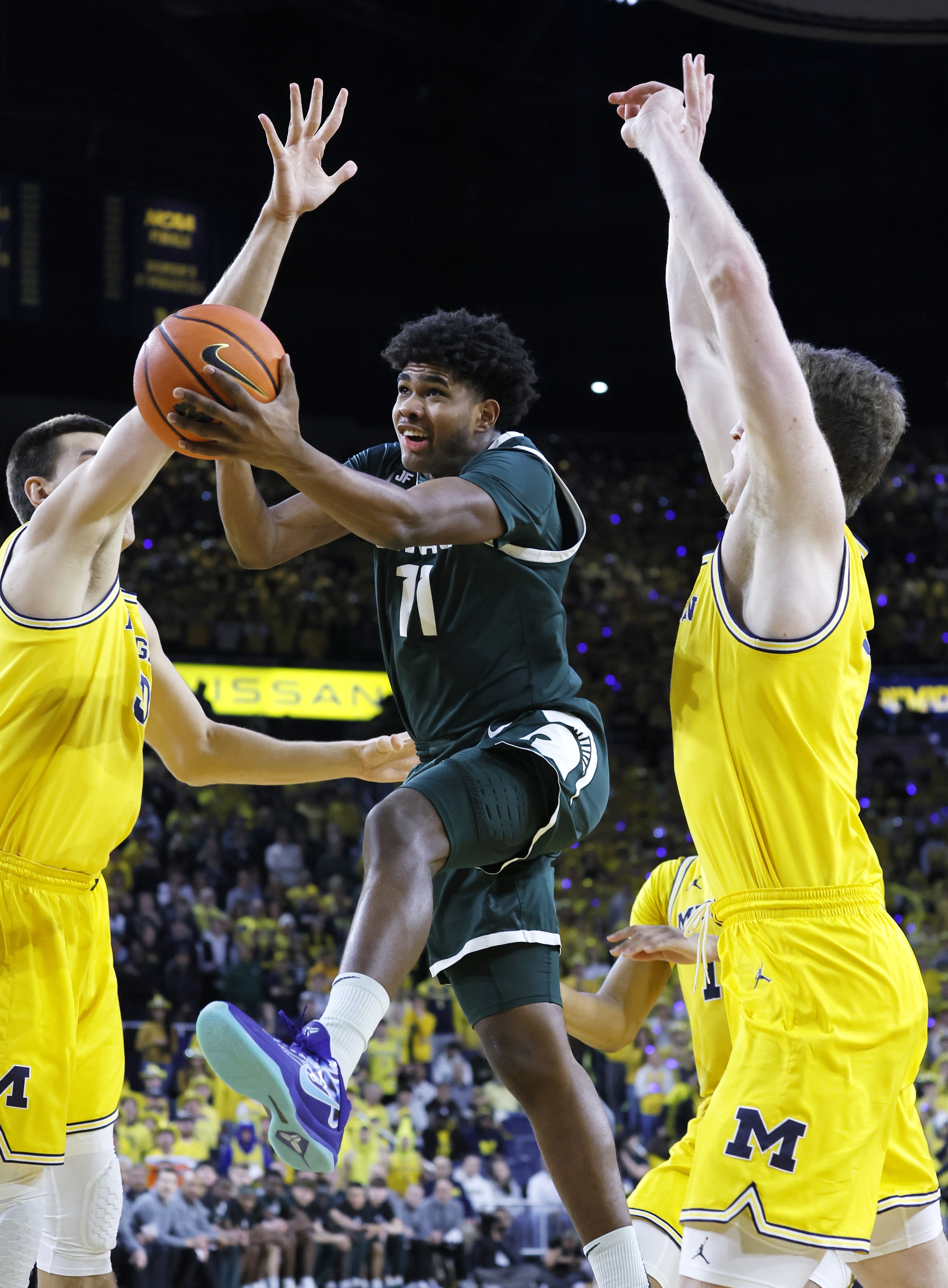 Michigan State guard Jase Richardson, center, goes to the basket between Michigan center Vladislav Goldin, left, and center Danny Wolf, right, during the first half of an NCAA college basketball game Friday, Feb. 21, 2025, in Ann Arbor, Mich. 