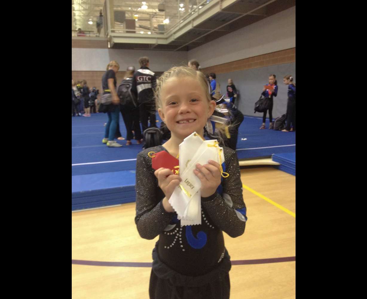 A young Avery Neff poses with several ribbons from a gymnastics competition.