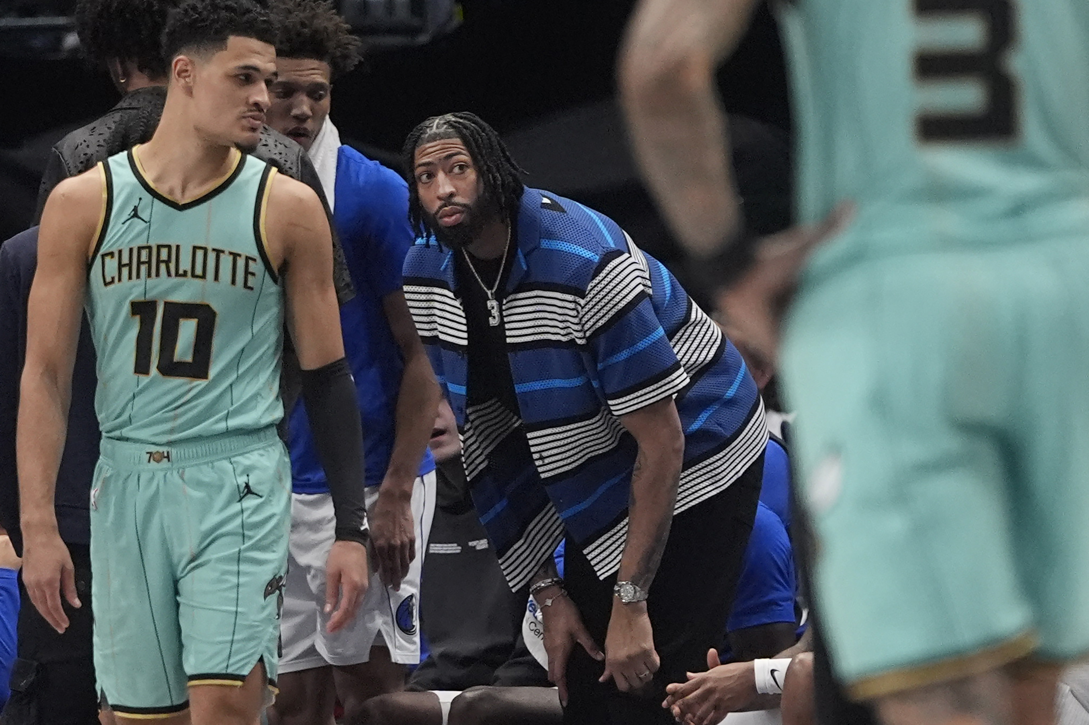 An injured Dallas Mavericks forward Anthony Davis, center, looks on from the sidelines as Charlotte Hornets guards Josh Green (10) and DaQuan Jeffries (3) stand on the court during the first half of an NBA basketball game in Dallas, Thursday, Feb. 27, 2025. 