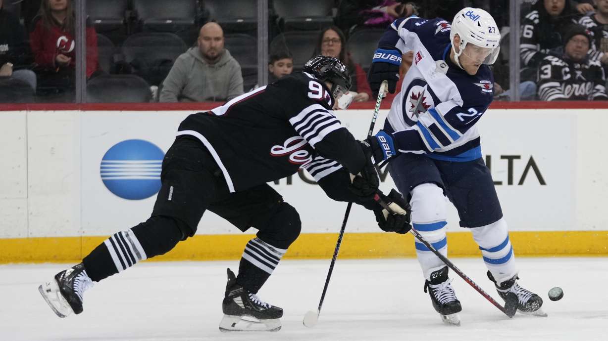 New Jersey Devils' Tomas Tatar, left, fights for control of the puck with Winnipeg Jets' Nikolaj Ehlers (27) during the first period of an NHL hockey game Friday, March 7, 2025, in Newark, N.J.