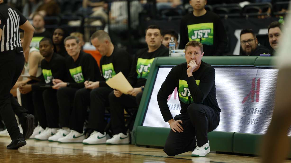 Utah Valley Men's Basketball coaching staff looking on while sporting 'JST' shirts in honor of President Astrid Tuminez late husband, Jeffery Tolk.