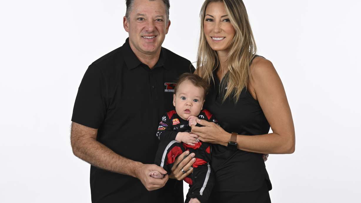 In this photo provided by the National Hot Rod Association, drivers Tony Stewart, left, and Leah Pruett hold their son, Dominic, during NHRA media day on Thursday, March 6, 2025.