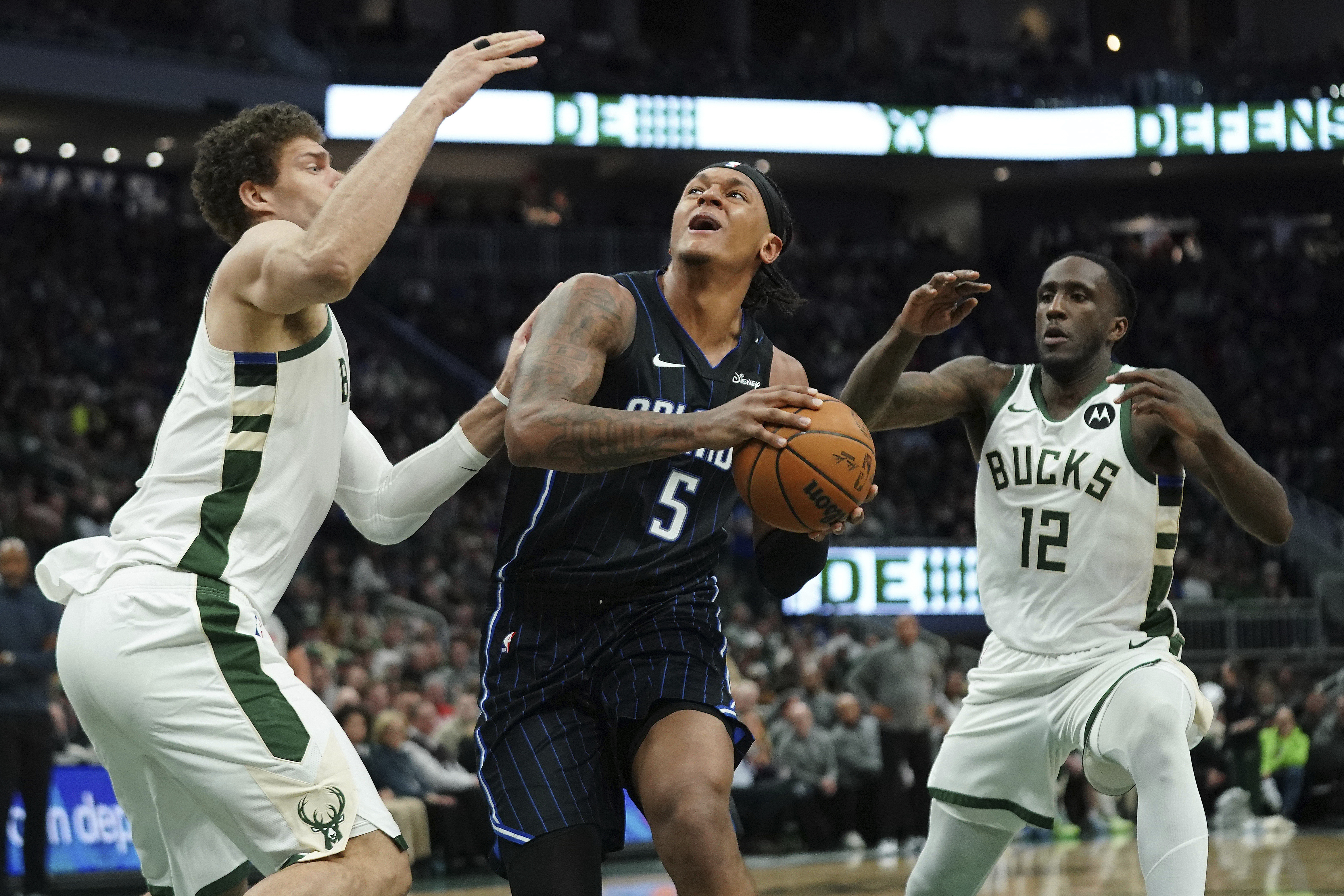 Orlando Magic's Paolo Banchero (5) drives to the basket between Milwaukee Bucks' Taurean Prince (12) and Brook Lopez, left, during the first half of an NBA basketball game Saturday, March 8, 2025, in Milwaukee. 