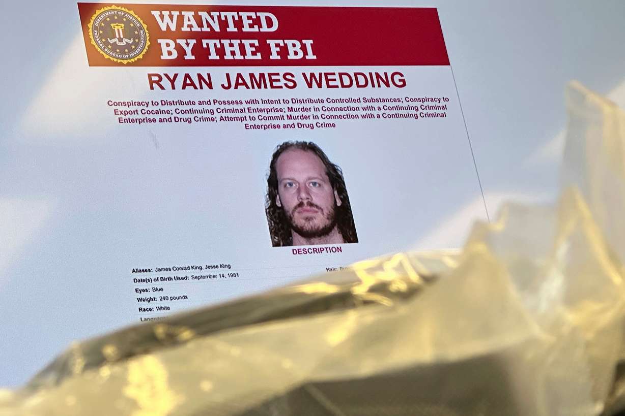 An image of former Canadian Olympic snowboarder Ryan Wedding, 43, who is a fugitive and has been charged with allegedly running and participating in a transnational drug trafficking operation, is displayed on a video monitor along with bricks of cocaine, foreground, during a news conference at the FBI offices in Los Angeles, Oct. 17, 2024.