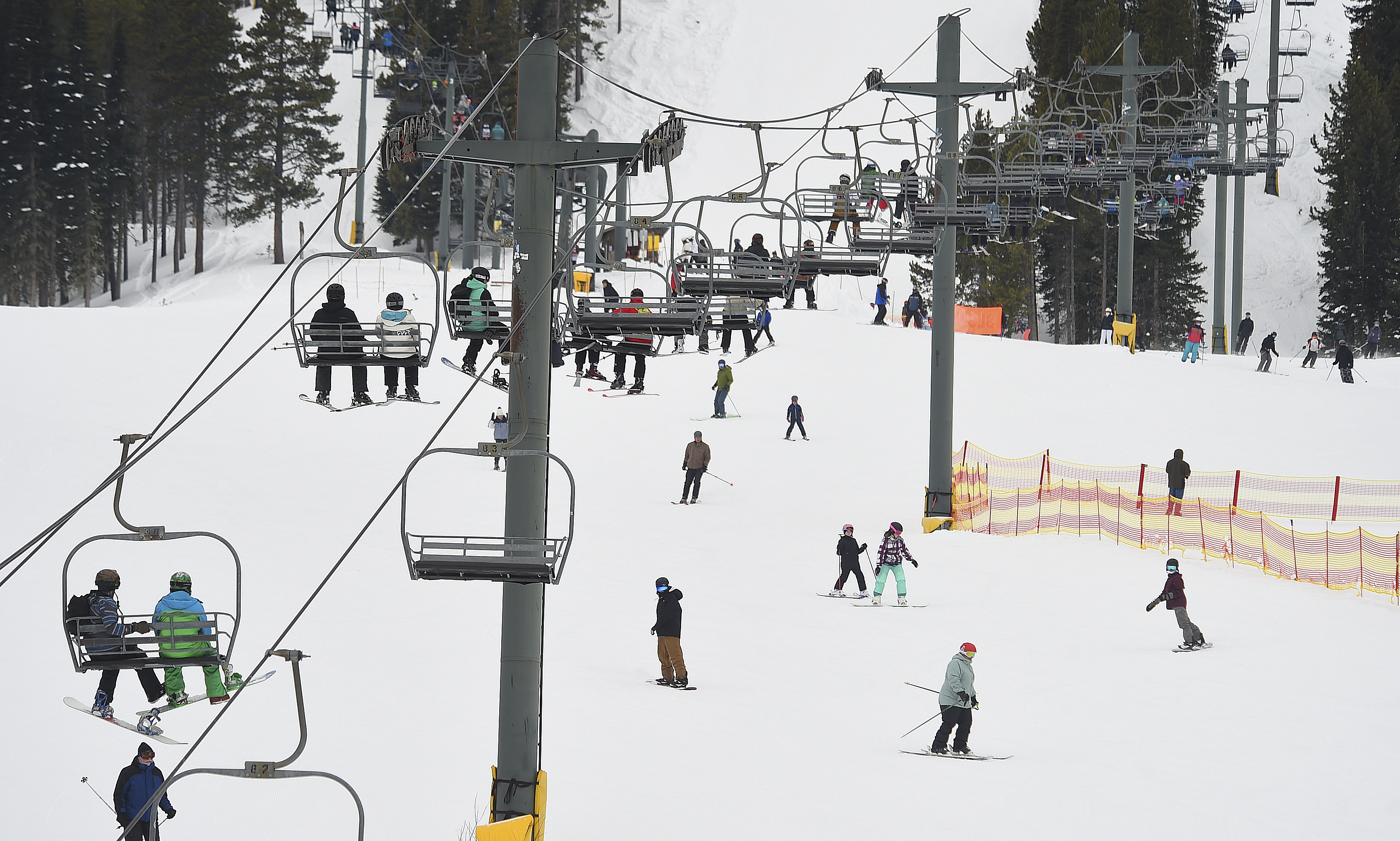People are seen riding a chairlift as skiers and snowboarders pass below at Red Lodge Mountain, Feb. 20, 2023, near Red Lodge, Mont. A man died after falling from a chairlift that was having a mechanical problem at the resort Monday.