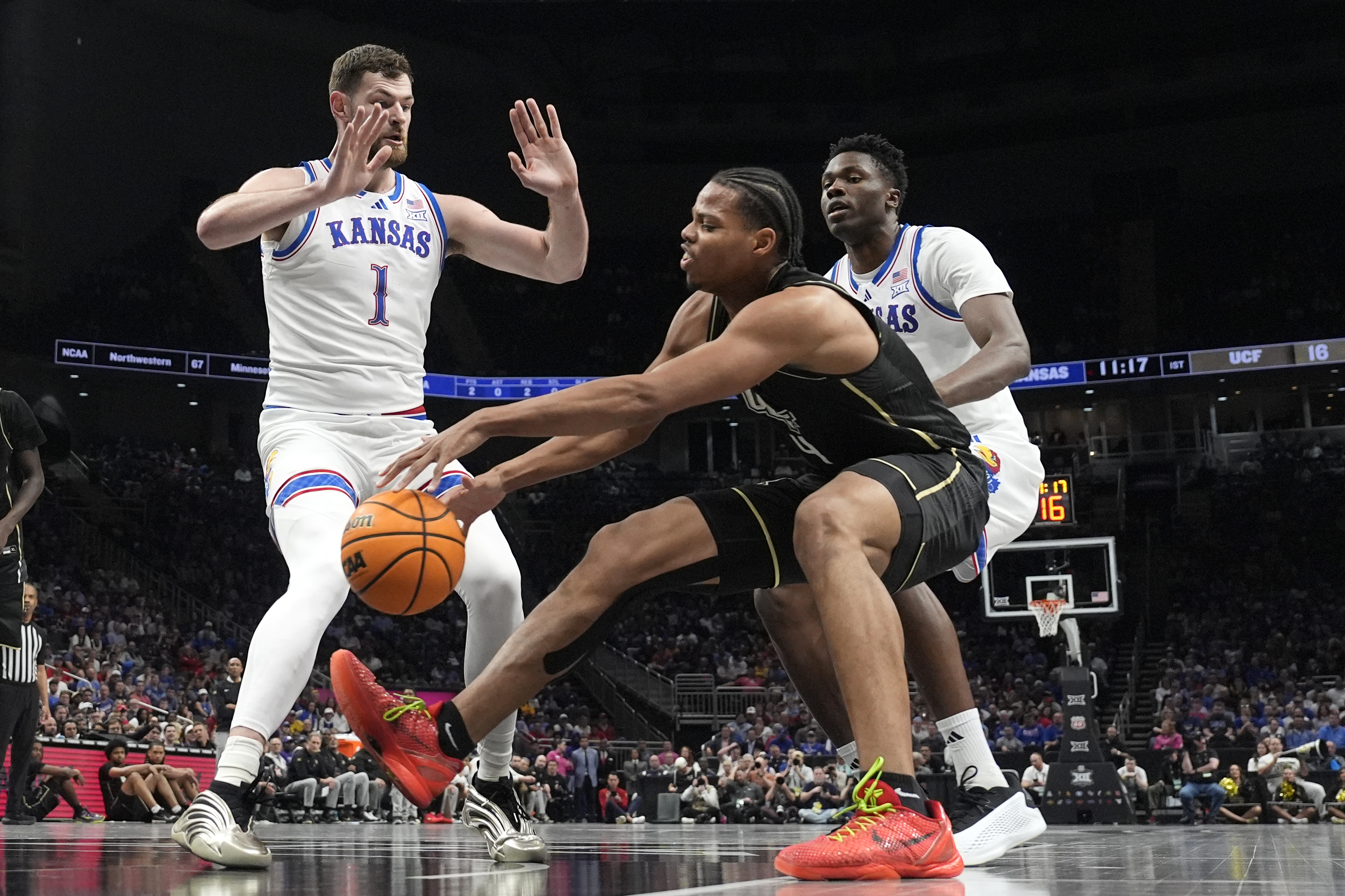 UCF's Keyshawn Hall (4) chases a loose ball as Kansas' Hunter Dickinson (1) and Flory Bidunga, right, defend during the first half of an NCAA college basketball game in the second round of the Big 12 Conference tournament, Wednesday, March 12, 2025, in Kansas City, Mo. 