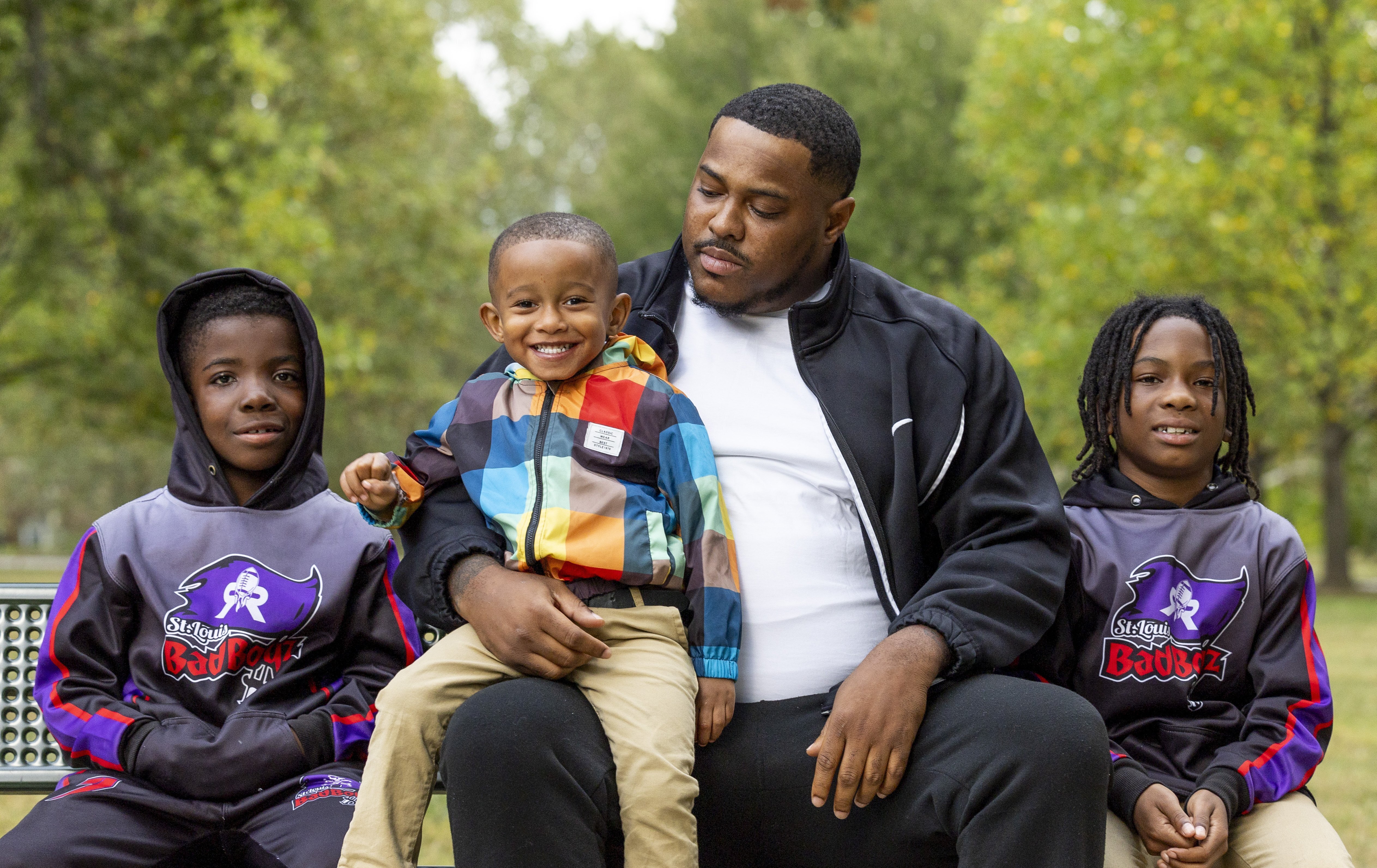 Shaquille Latimore, second from right, sits with two players on the youth football league he assistant coaches at a park in south St. Louis on Thursday, Oct. 19, 2023.