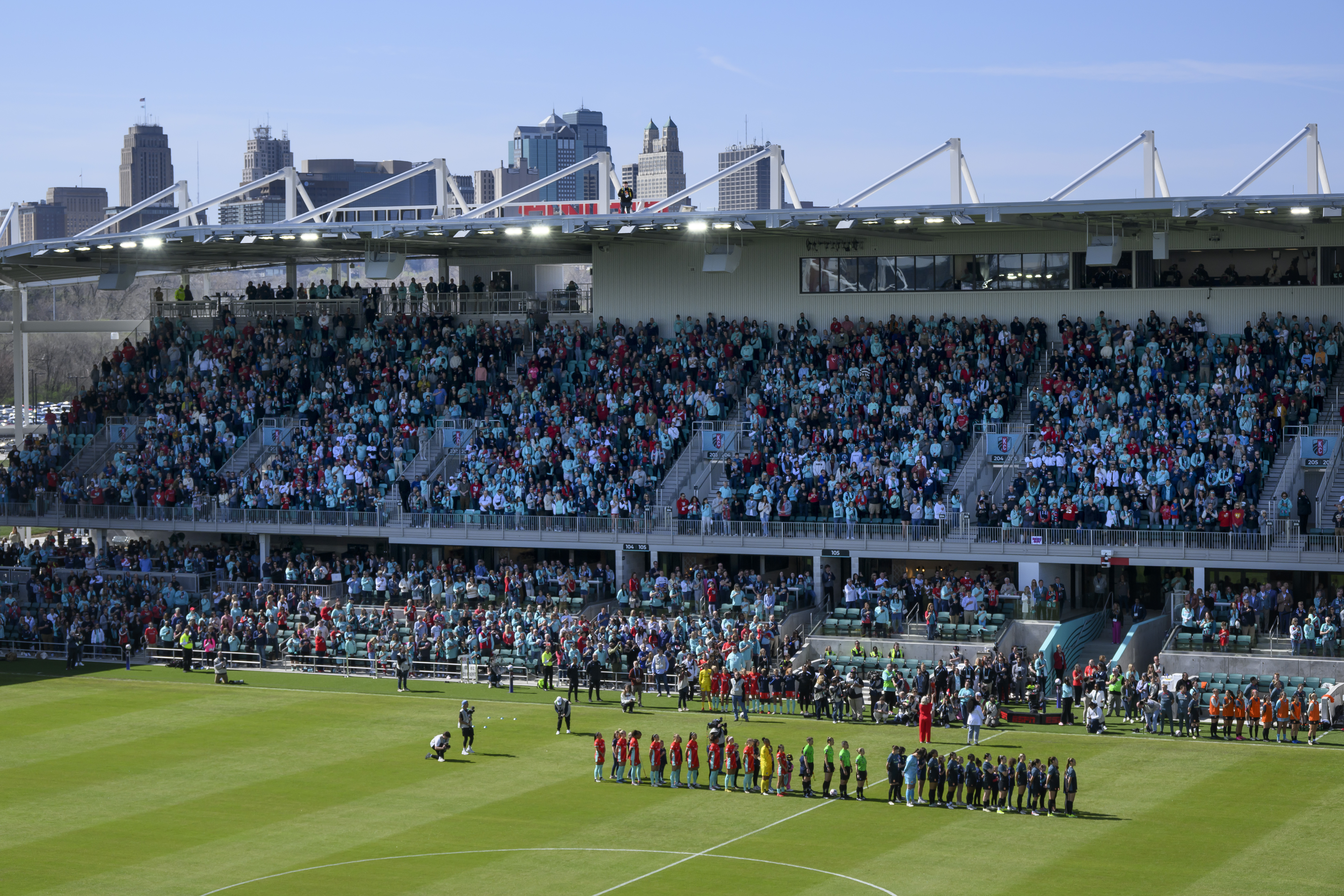 FILE - With the skyline of Kansas City behind them, the Kansas City Current and the Portland Thorns FC line up before the start of an NWSL soccer match at the new CPKC Stadium, March 16, 2024, in Kansas City, Mo.