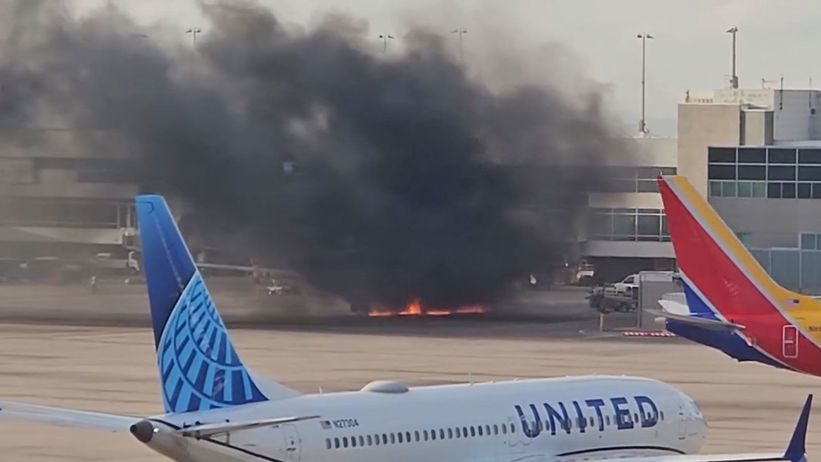 A frame from a video shows flames under a plane and black smoke rising at the Denver airport on Thursday. An engine caught fire on an American Airlines plane.