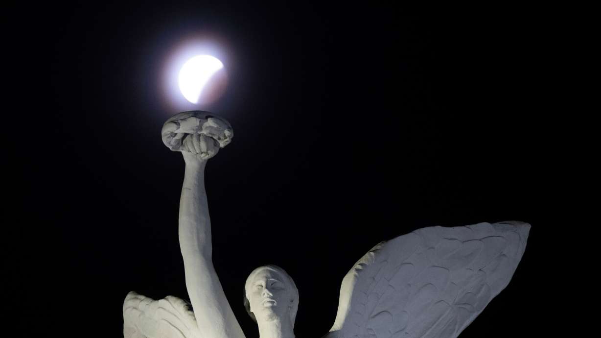 The blood moon lunar eclipse is seen behind a statue on the Princes' Gates in Toronto on Friday.