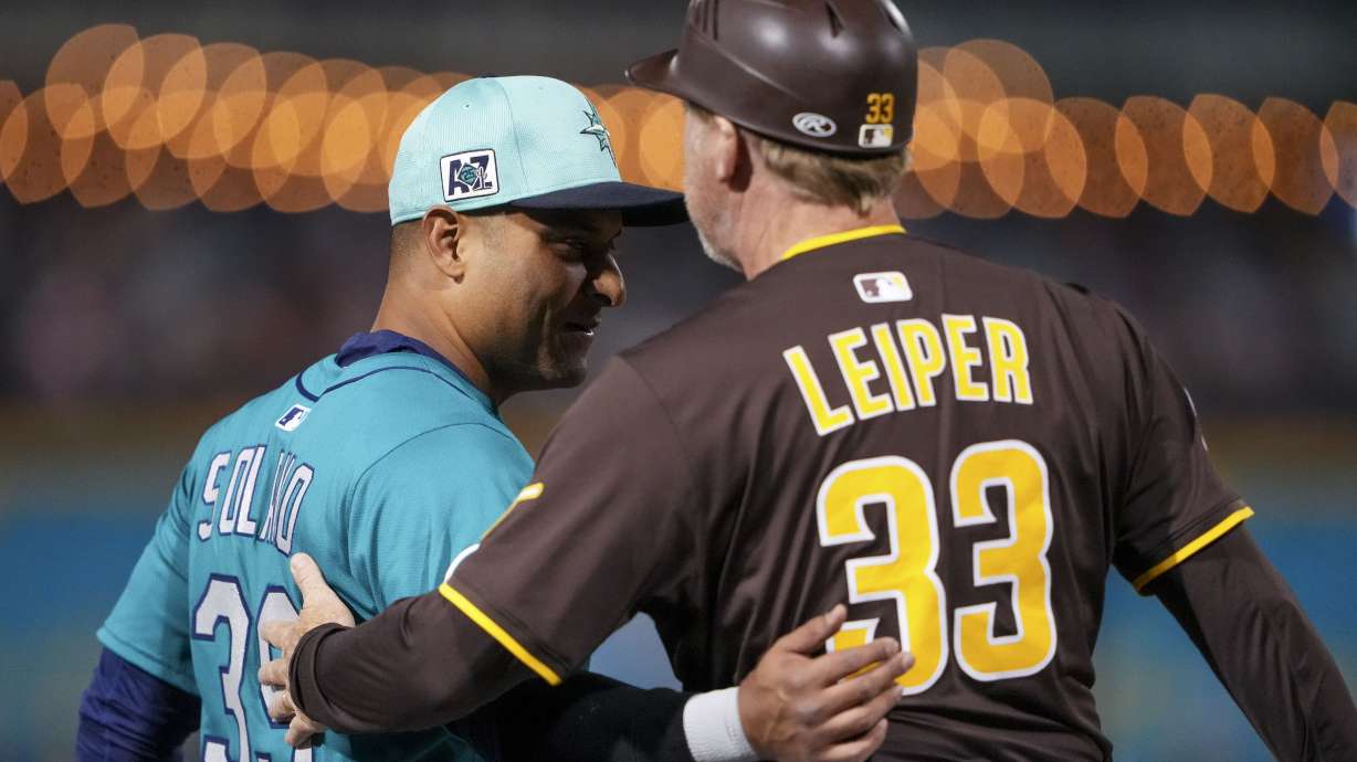 Seattle Mariners third baseman Donovan Solano, left, greets San Diego Padres third base coach, infield & base running instructor Tim Leiper, right, during a spring training baseball game Friday, Feb. 28, 2025, in Peoria, Ariz.