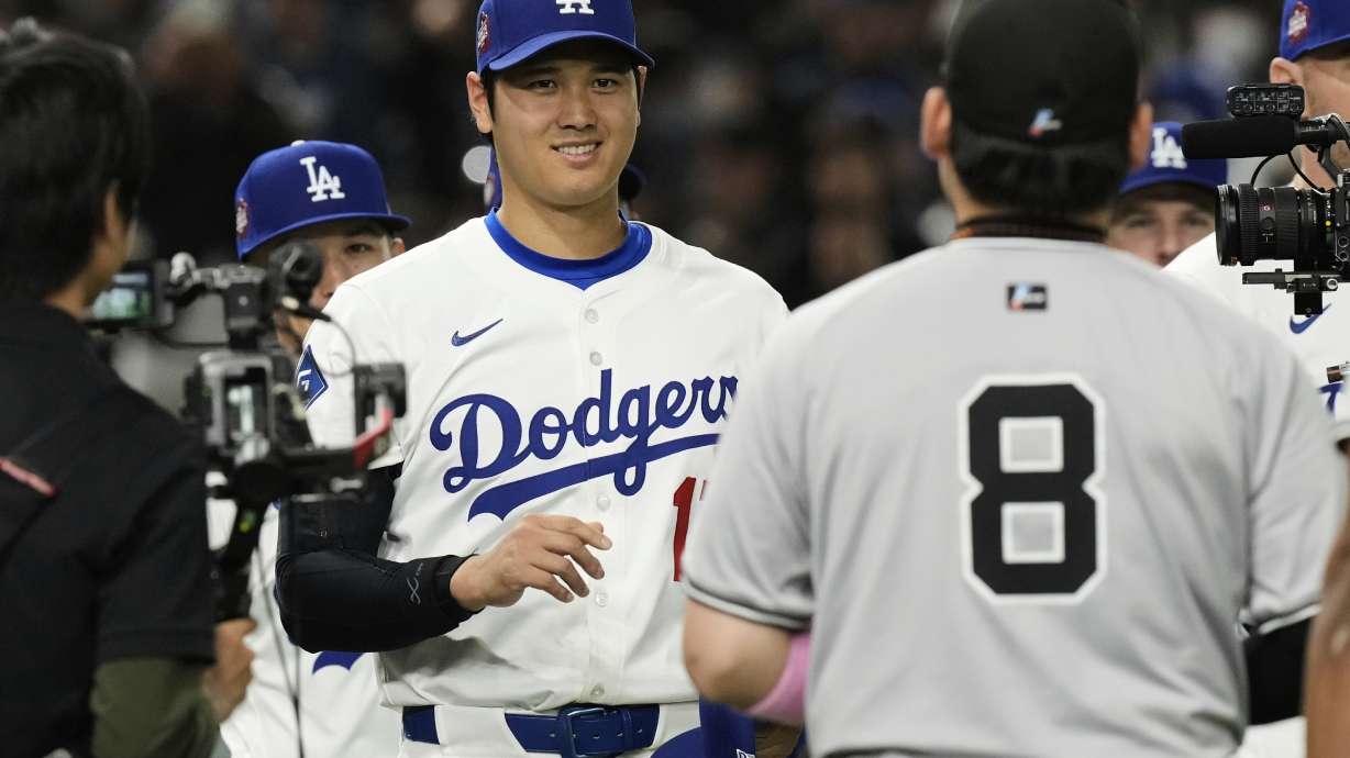 Los Angeles Dodgers' Shohei Ohtani, left, and Yomiuri Giants' Yoshihiro Maru, front, greet each other before the first inning of a spring training baseball game in Tokyo, Japan, Saturday, March 15, 2025.