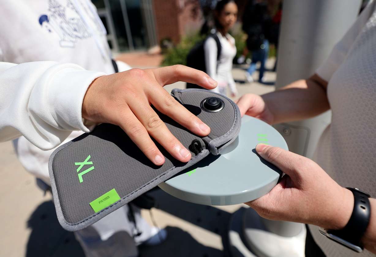 A student unlocks a Yondr pouch that has his cell phone inside on a magnetic unlocking base as he leaves Granger High School in West Valley City on Aug. 26, 2024. Students lock their phones in the pouches when they arrive at school, creating a phone-free learning environment.