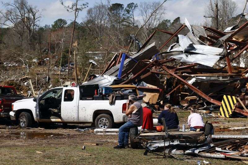 Friends and family members take a break as they search for belongings in the damage after a tornado passed through the area, Sunday in Plantersville, Ala.