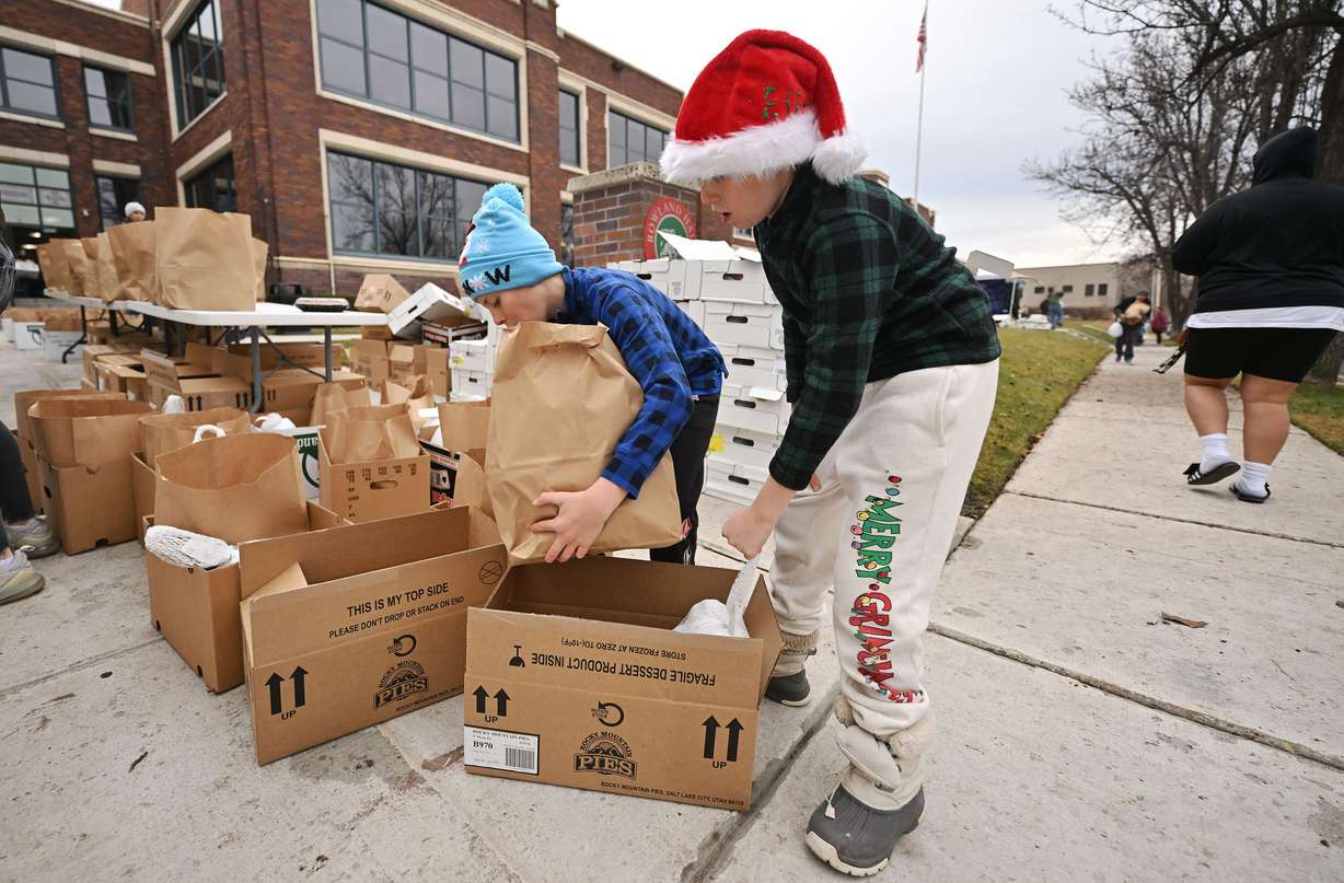 Brothers Walty and Will Wucetich get boxes of food ready to put into cars as they pull up as Crossroads Urban Center and volunteers gather at Rowland Hall to hand out 1,000 bags of food and turkeys to families in Salt Lake City on Dec. 23, 2024.