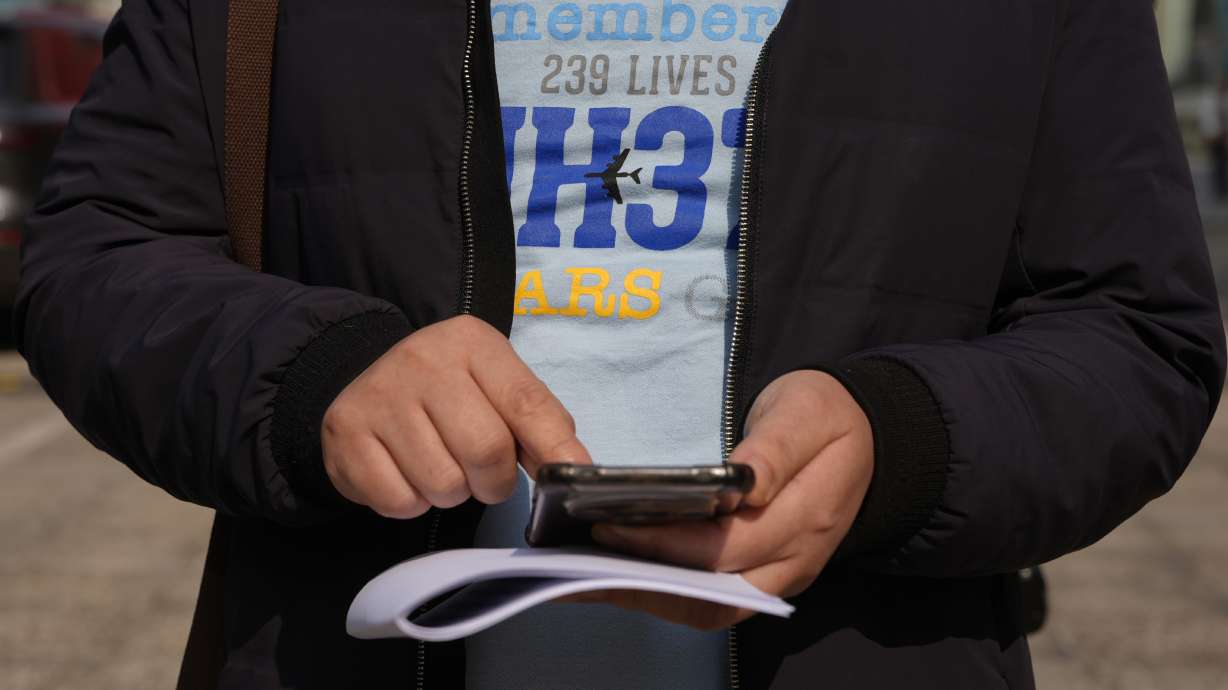 Jiang Hui, whose mother was on the missing MH370 Malaysia Airline passenger jet, wears a shirt "Remembering 239 Lives, MH370" and checks his phone after talking to media on the 11th anniversary of the jet going missing March 8 in Beijing, China.