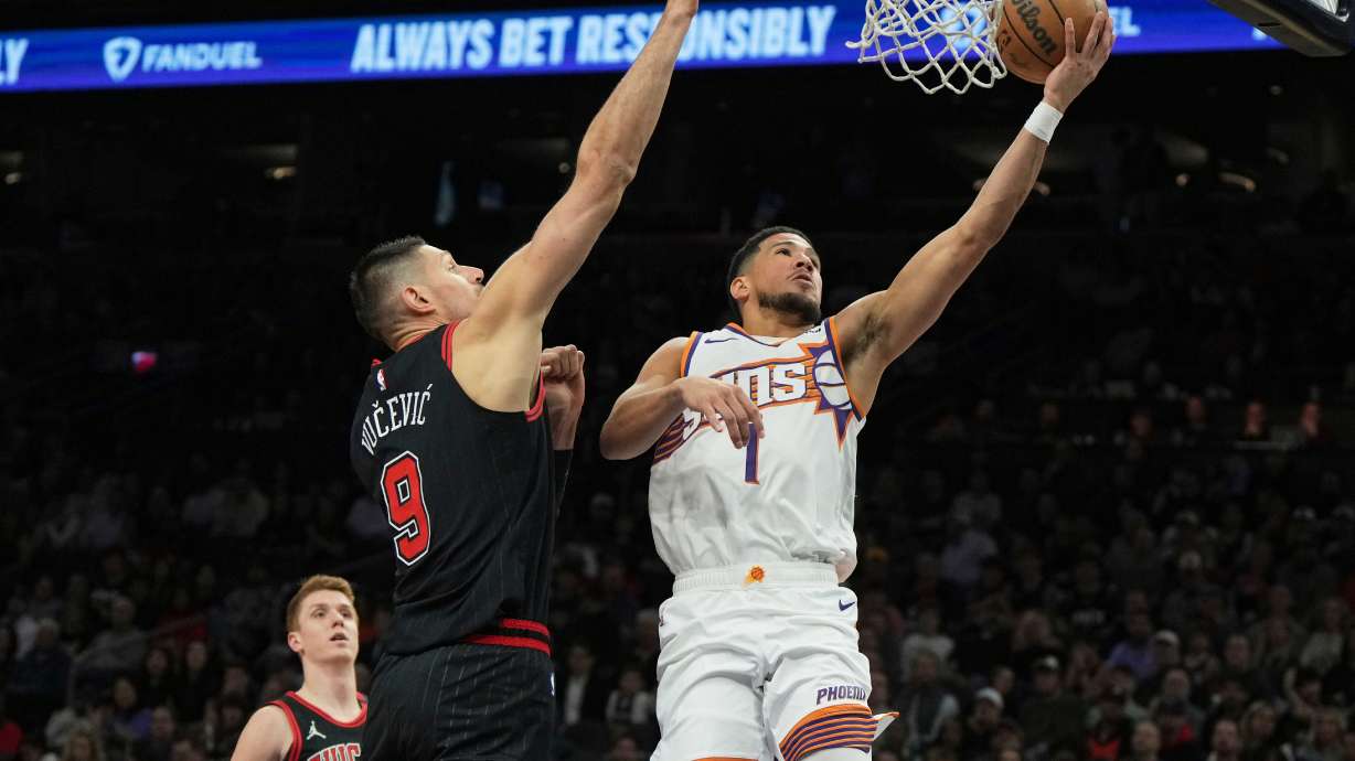 Phoenix Suns guard Devin Booker (1) drives against Chicago Bulls center Nikola Vucevic during the first half of an NBA basketball game, Wednesday, March 19, 2025, in Phoenix.