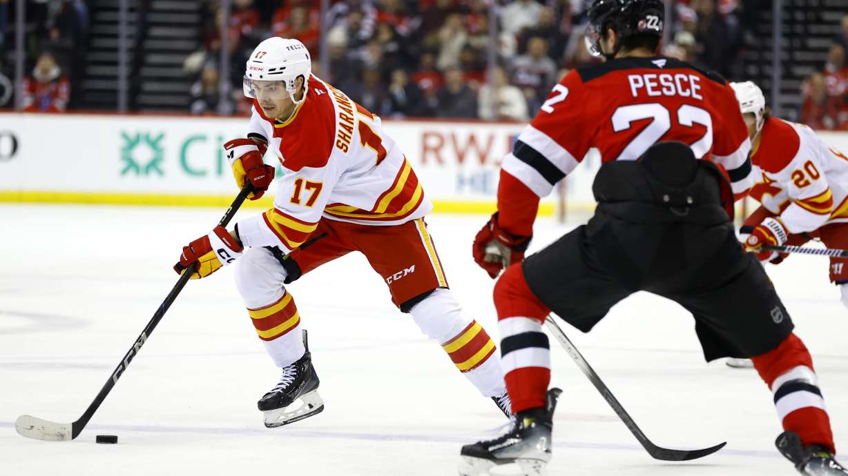 Calgary Flames center Yegor Sharangovich (17) controls the puck in front of New Jersey Devils defenseman Brett Pesce (22) during the first period of an NHL hockey game, Thursday, March 20, 2025, in Newark, N.J.