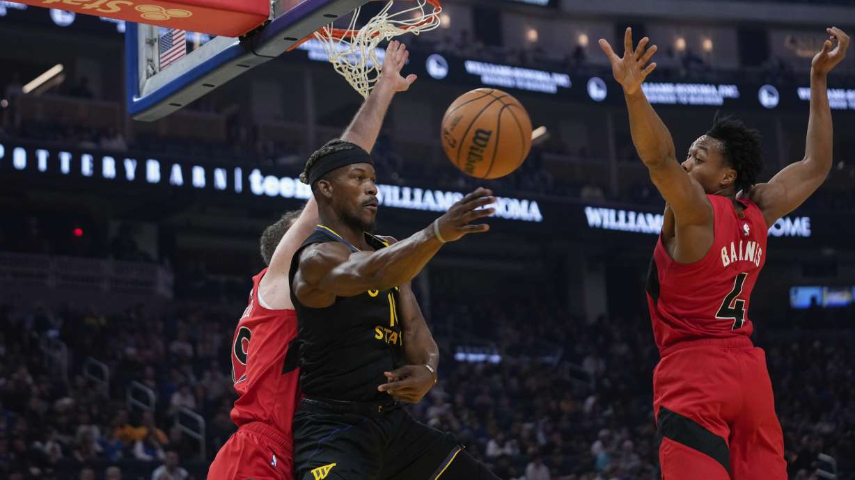 Golden State Warriors forward Jimmy Butler III, center, passes the ball between Toronto Raptors center Jakob Poeltl, left, and guard Scottie Barnes during the first half of an NBA basketball game Thursday, March 20, 2025, in San Francisco.