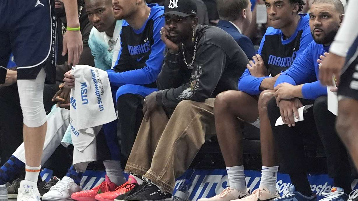 An injured Dallas Mavericks guard Kyrie Irving, center, sits on the bench between teammates Dwight Powell, left, and Max Christie (00) during the first half of an NBA basketball game against the Philadelphia 76ers in Dallas, Sunday, March 16, 2025.