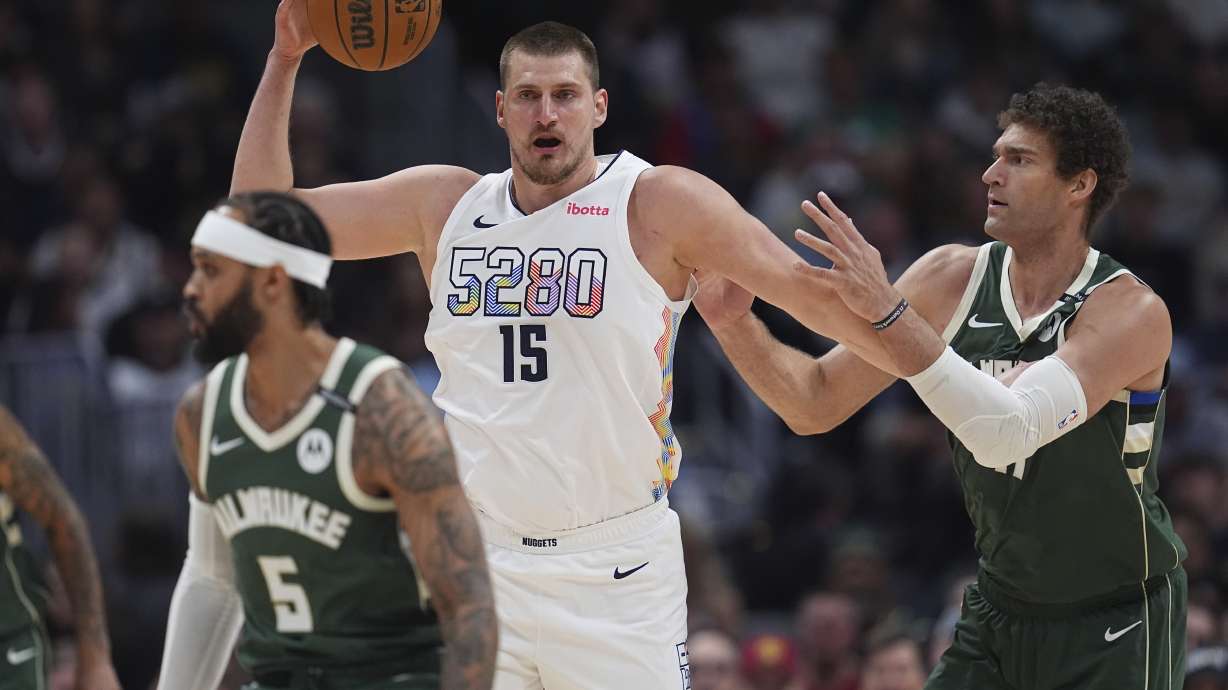 Denver Nuggets center Nikola Jokic, left, fields a pass as Milwaukee Bucks center Brook Lopez defends in the first half of an NBA basketball game Wednesday, March 26, 2025, in Denver.