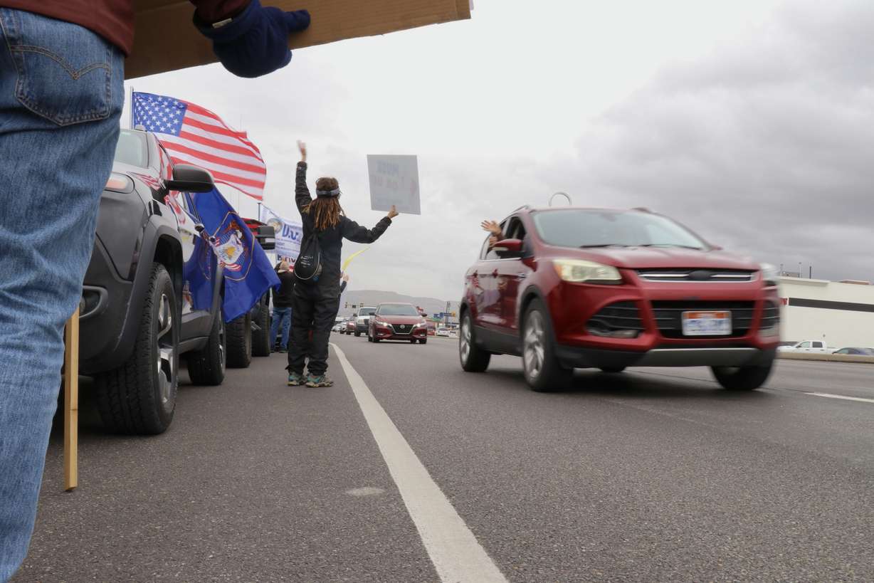 Protesters waive signs outside a Tesla dealership in South Salt Lake during a demonstration on Saturday.