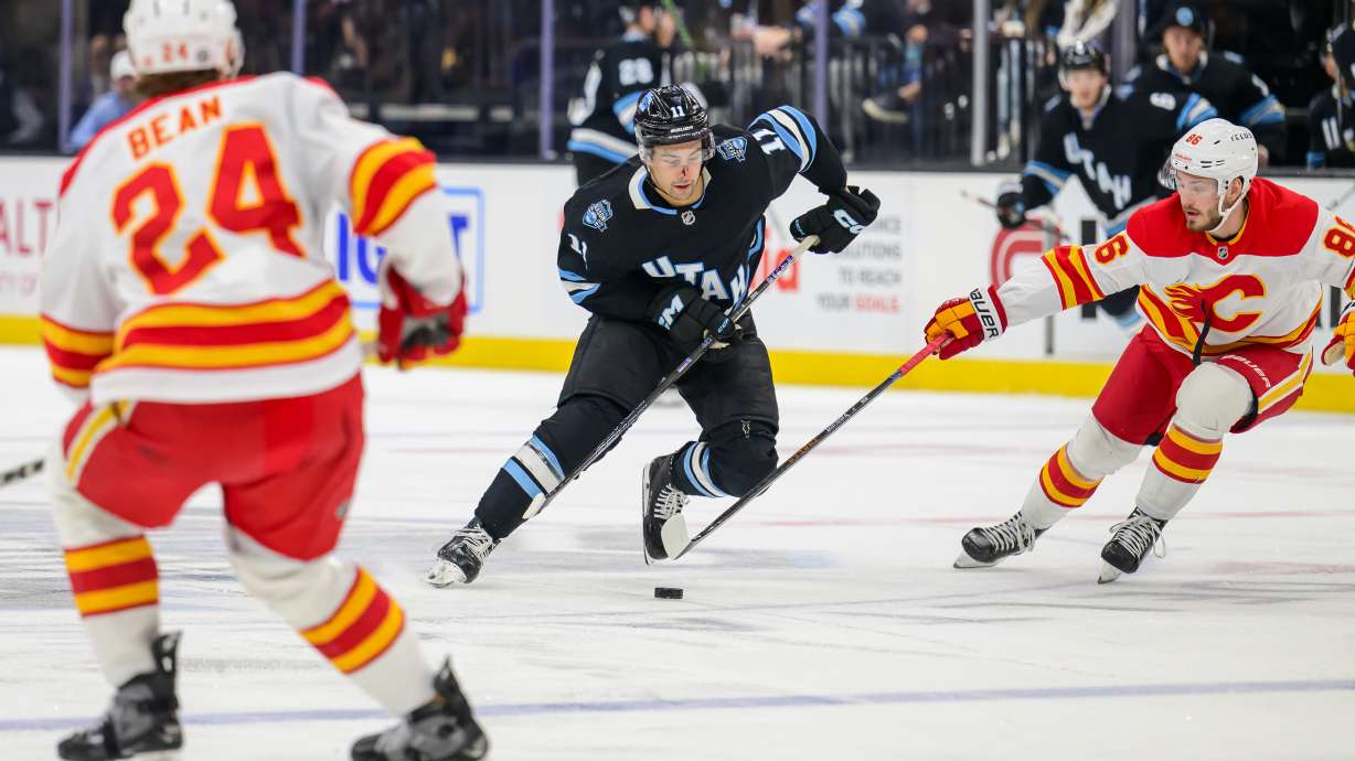 Utah Hockey Club right wing Dylan Guenther (11) skates the puck through the defense of Calgary Flames left wing Joel Farabee (86) and Calgary Flames defenseman Jake Bean (24) during the third period of an NHL hockey game Tuesday, April 1, 2025, in Salt Lake City.