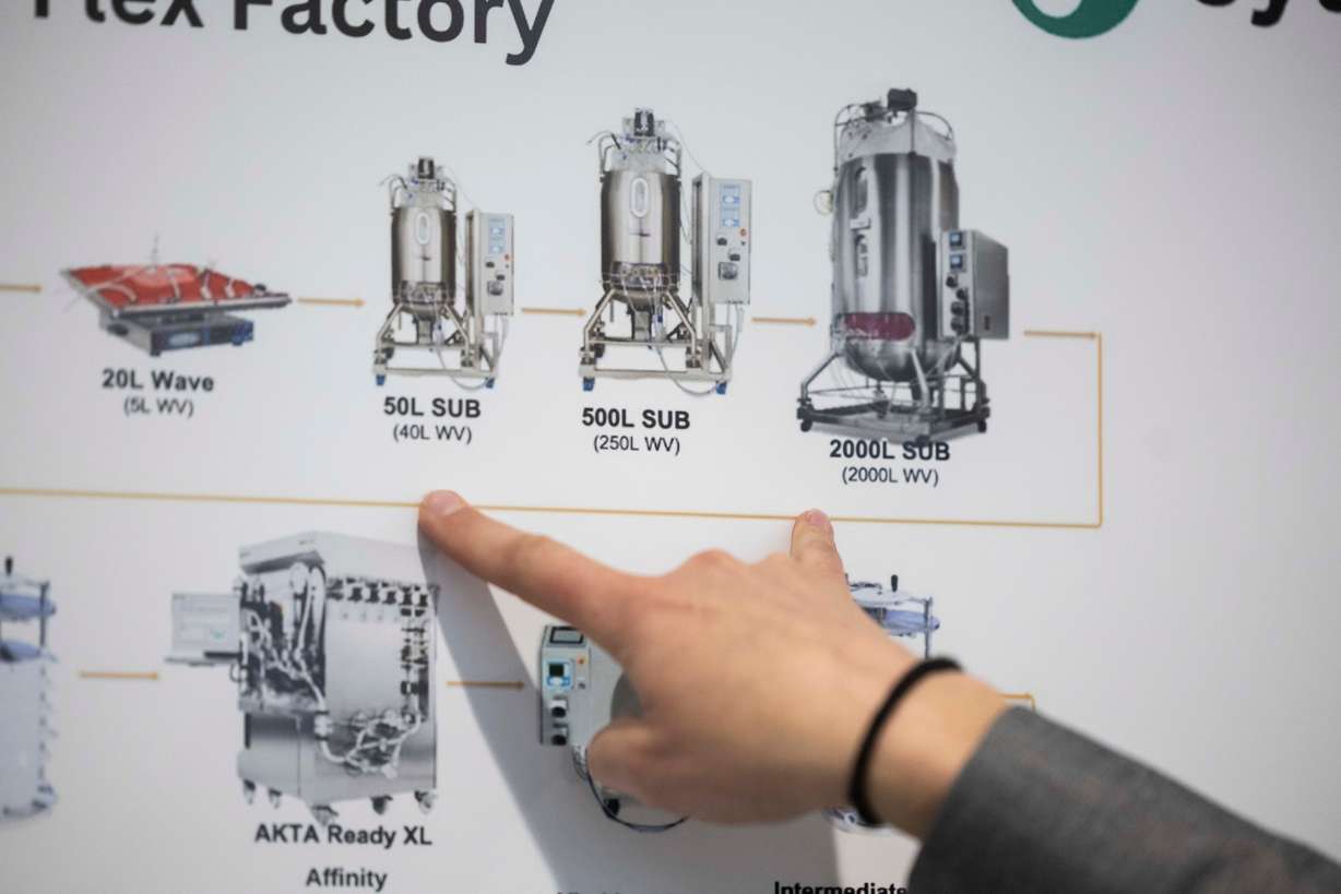 Nikki Castignani, the associate director of business operations and materials management for Denali Therapeutics’ Salt Lake City location, points to different sizes of bioreactors on a chart during a ribbon cutting for Denali Therapeutics' new biomedical facility in Salt Lake City on March 27.