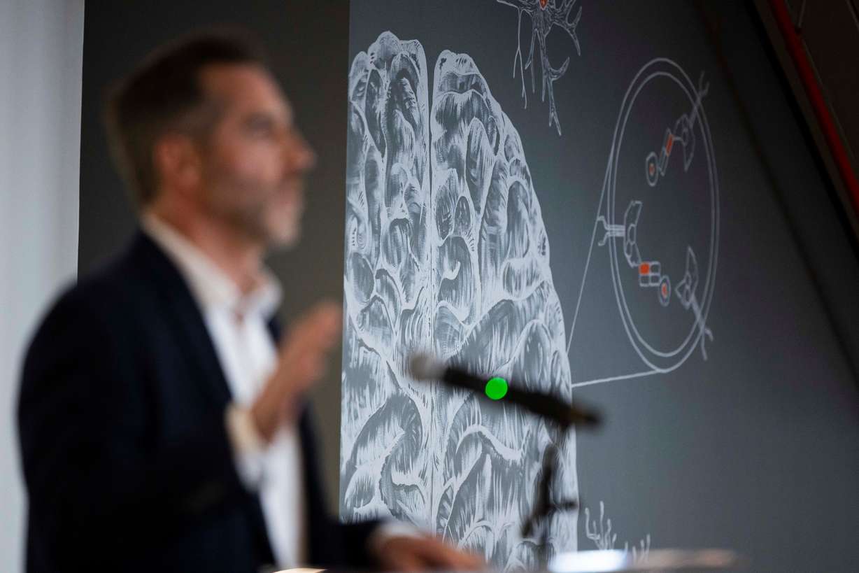 A mural on the wall that depicts medicines crossing the brain-blood barrier is pictured while Denali Therapeutics chief executive officer Ryan Watts speaks during a ribbon cutting for Denali Therapeutics' new biomedical facility in Salt Lake City on March 27.