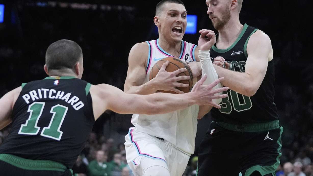Miami Heat guard Tyler Herro, center, drives to the basket between Boston Celtics forward Sam Hauser, right, and guard Payton Pritchard (11) during the second half of an NBA basketball game, Wednesday, April 2, 2025, in Boston.