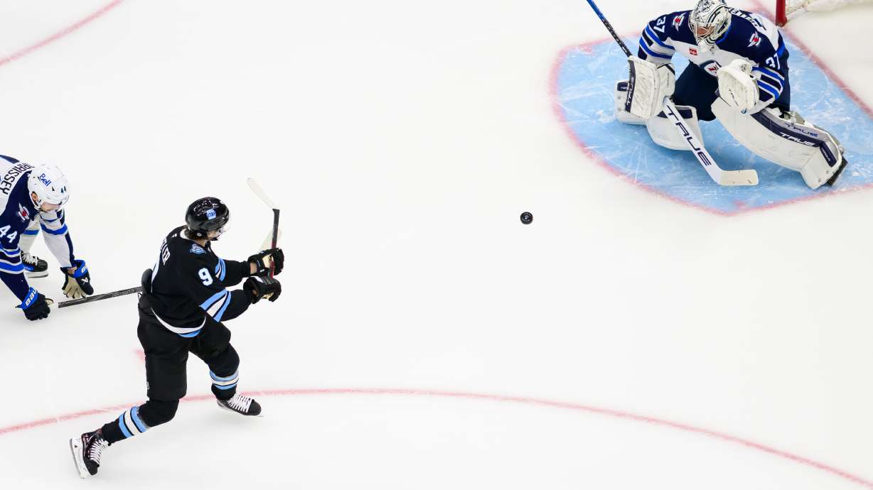 Utah Hockey Club center Clayton Keller (9) shoots the puck as Winnipeg Jets goaltender Connor Hellebuyck (37) protects the net during the first period of an NHL hockey game Saturday, April 5, 2025, in Salt Lake City.