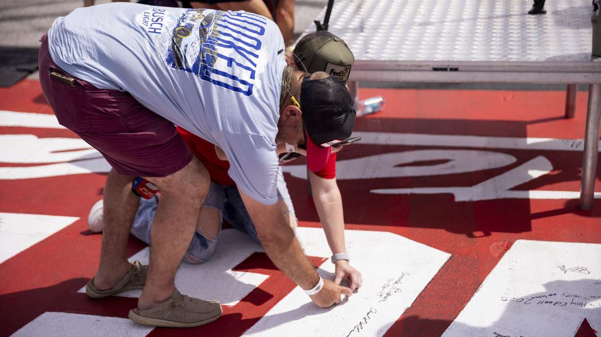 Fans sign the start/finish line at before a NASCAR Cup Series auto race at Darlington Raceway, Sunday, April 6, 2025, in Darlington, S.C.