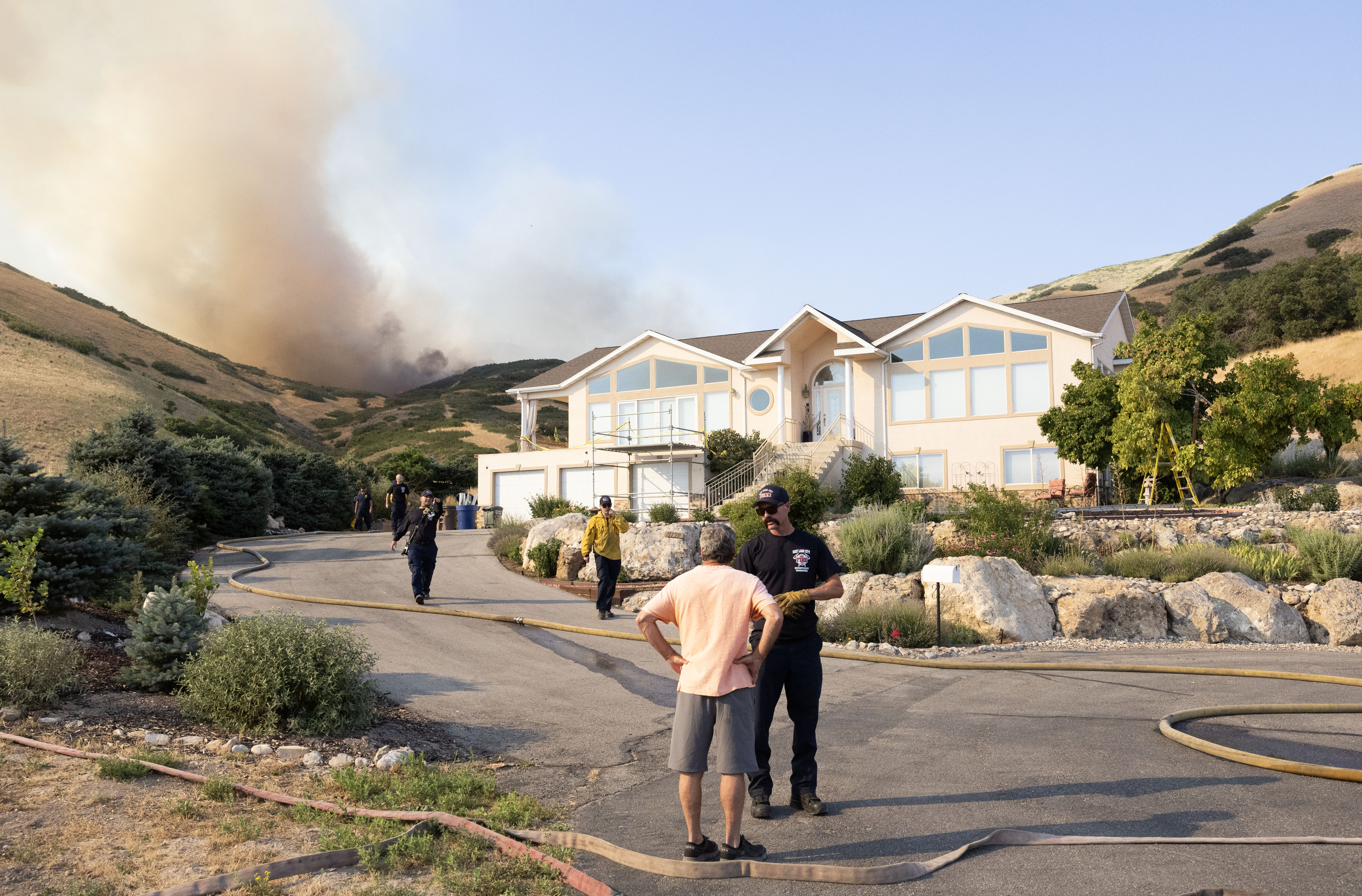 A Salt Lake firefighter tells a local resident to evacuate while the flames from a wildfire burning around Ensign Peak grow closer to his home on Twickenham Drive in Salt Lake City on July 20, 2024.